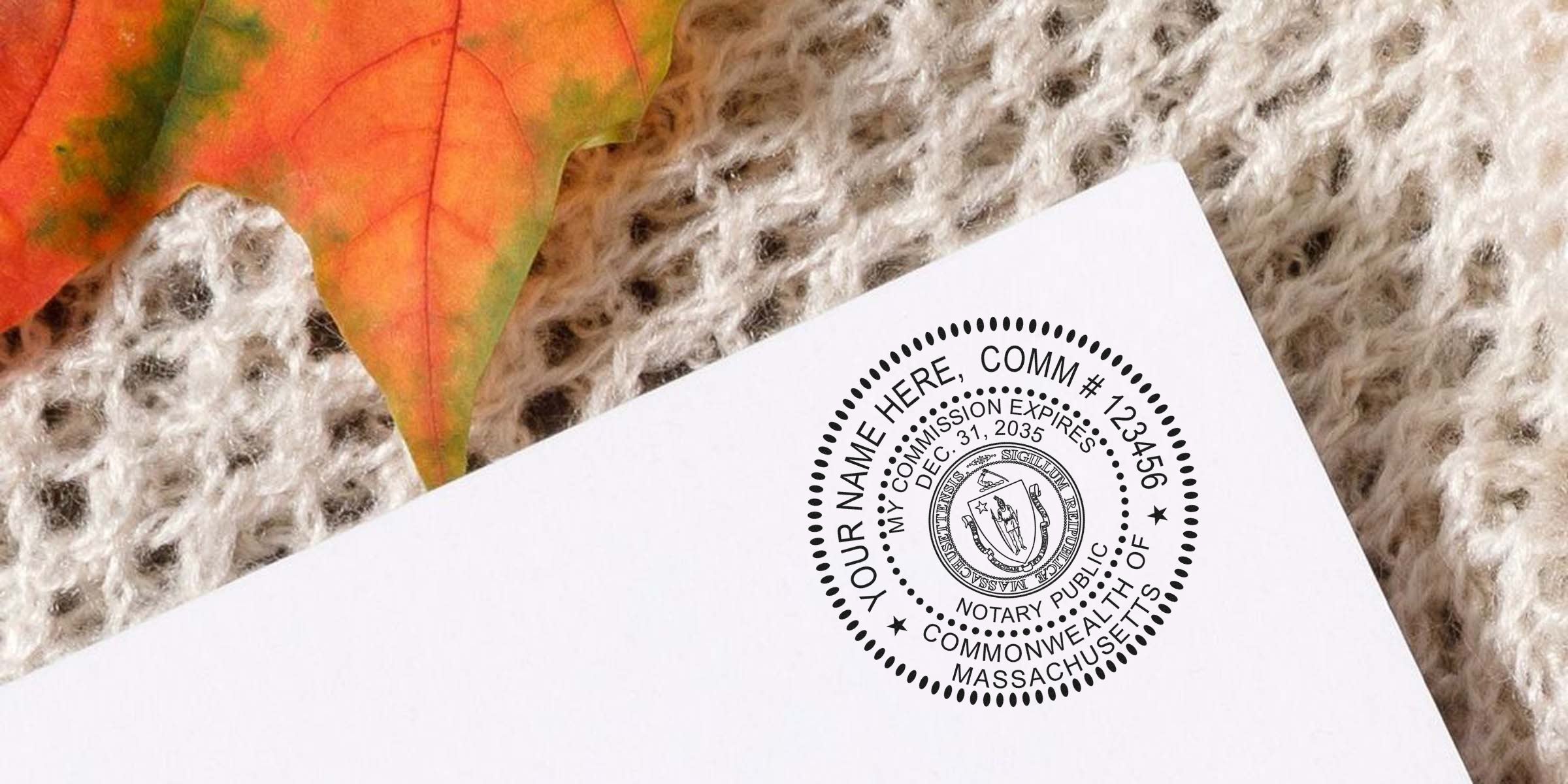 Close-up of a Massachusetts notary public round seal stamped on white paper, resting on cream knit fabric with an orange autumn leaf.