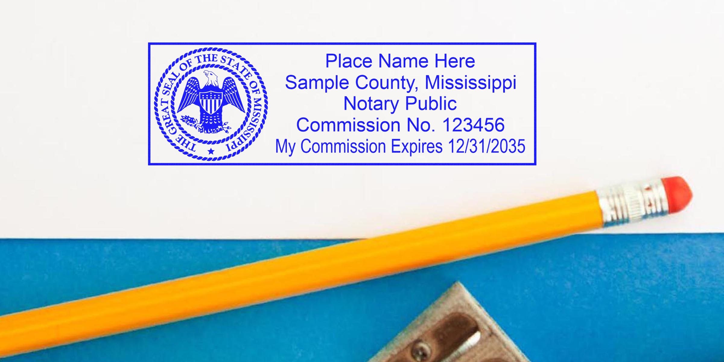 Blue Mississippi notary stamp on white paper showing state seal, sample county, commission number and expiration date, next to a yellow pencil and metal pencil sharpener on a blue background