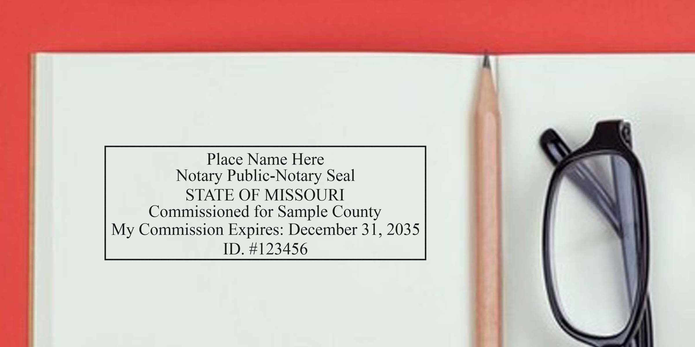Open notebook page showing a Missouri notary public seal mock-up with commission expiration date and ID number, placed beside a pencil and black eyeglasses on a red background