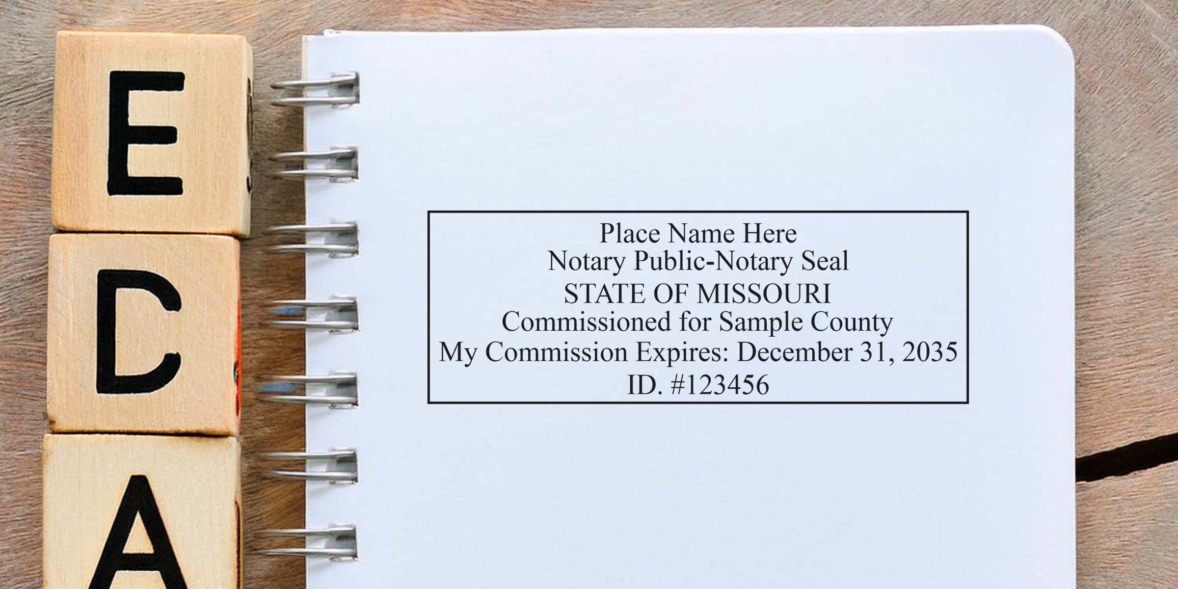 Spiral-bound notebook open to a blank page showing a boxed sample "State of Missouri" notary public seal and commission details, alongside stacked wooden letter blocks on a wooden tabletop.