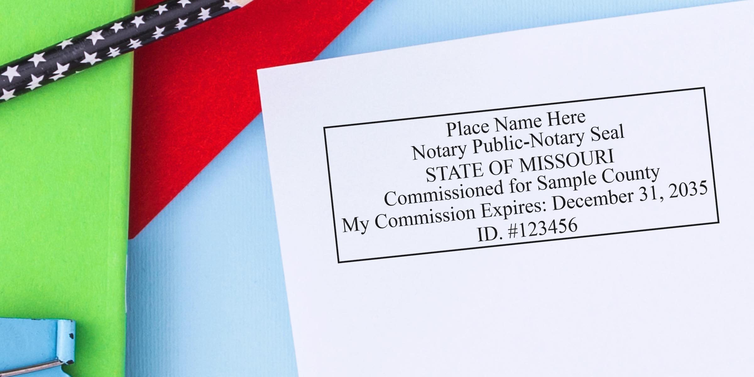 Close-up of a notary public notary seal sample for the State of Missouri printed on white paper, placed on blue, red, and green background with a black star-pattern pencil and binder clip — office document, notary stamp, legal paperwork.