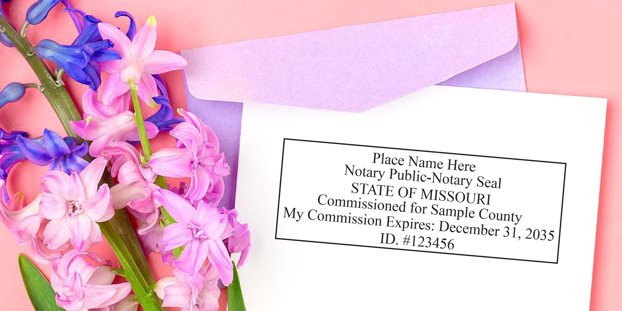 Flat lay of a purple envelope and white paper displaying a Missouri notary commission sample stamp beside pink and purple hyacinth flowers on a pastel pink background