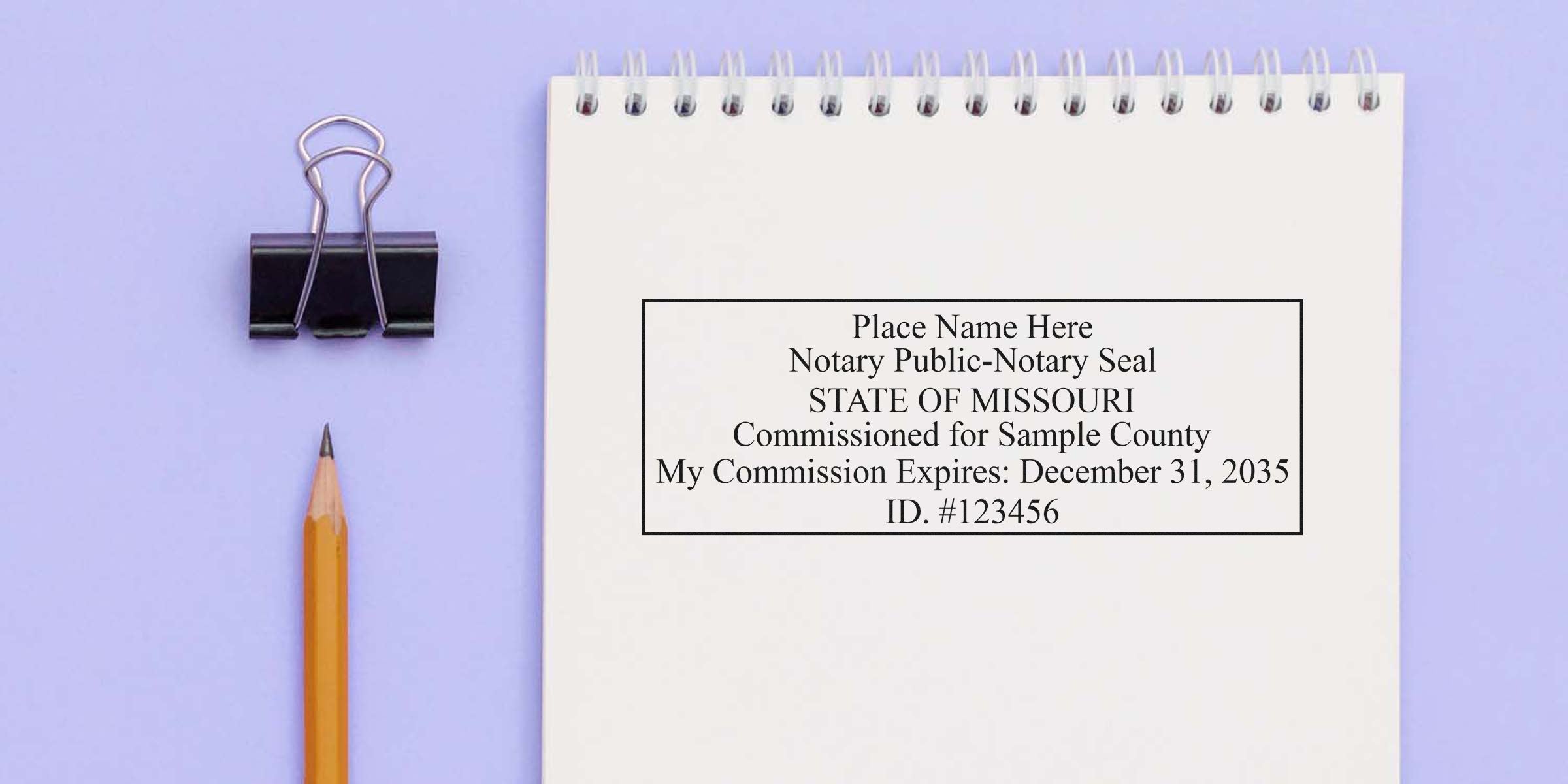Spiral notebook page showing a sample notary public seal for the State of Missouri with commission expiration date, pictured beside a yellow pencil and black binder clip on a light purple background.