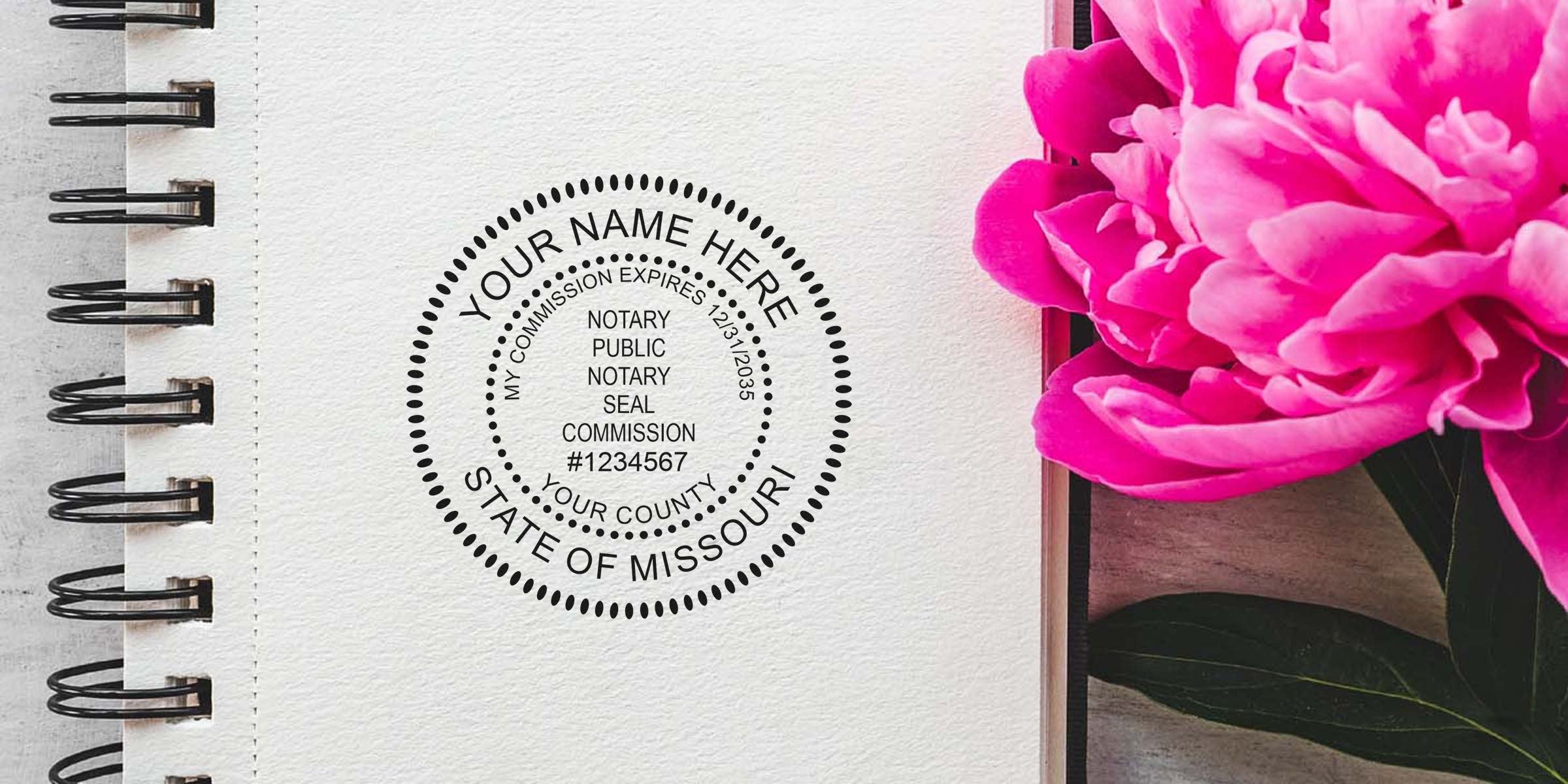 Spiral-bound notebook page with a black circular notary seal reading "State of Missouri" stamped beside a vibrant pink peony flower on a wooden surface.
