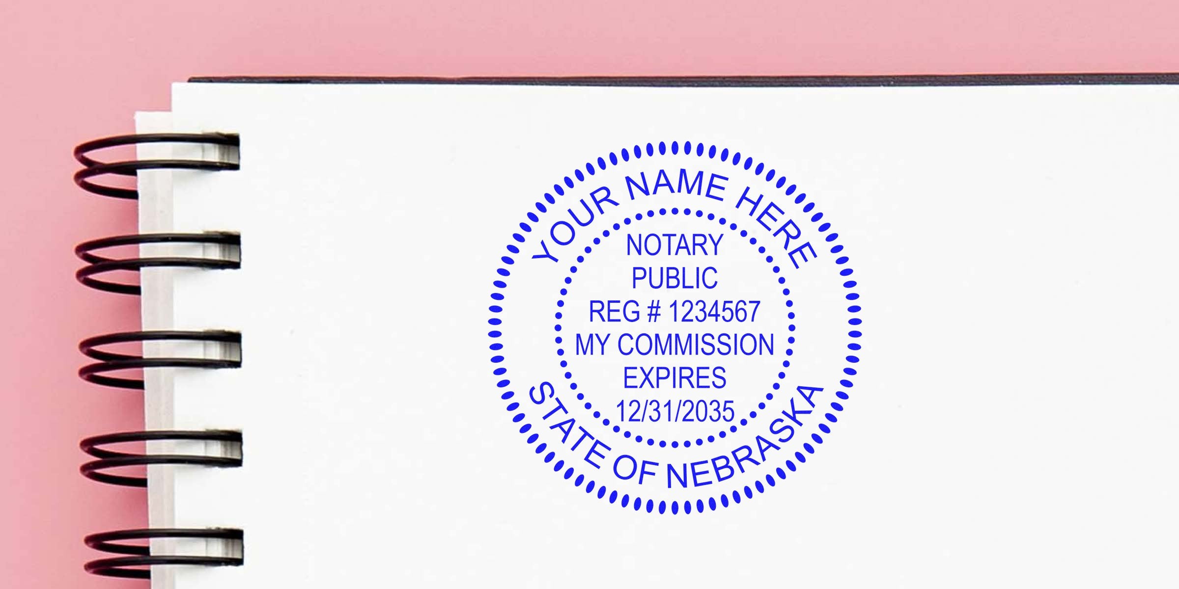 Blue circular notary public stamp mockup reading "Your Name Here, State of Nebraska" with reg# and commission expiry printed on a white spiral-bound notebook page against a pink background