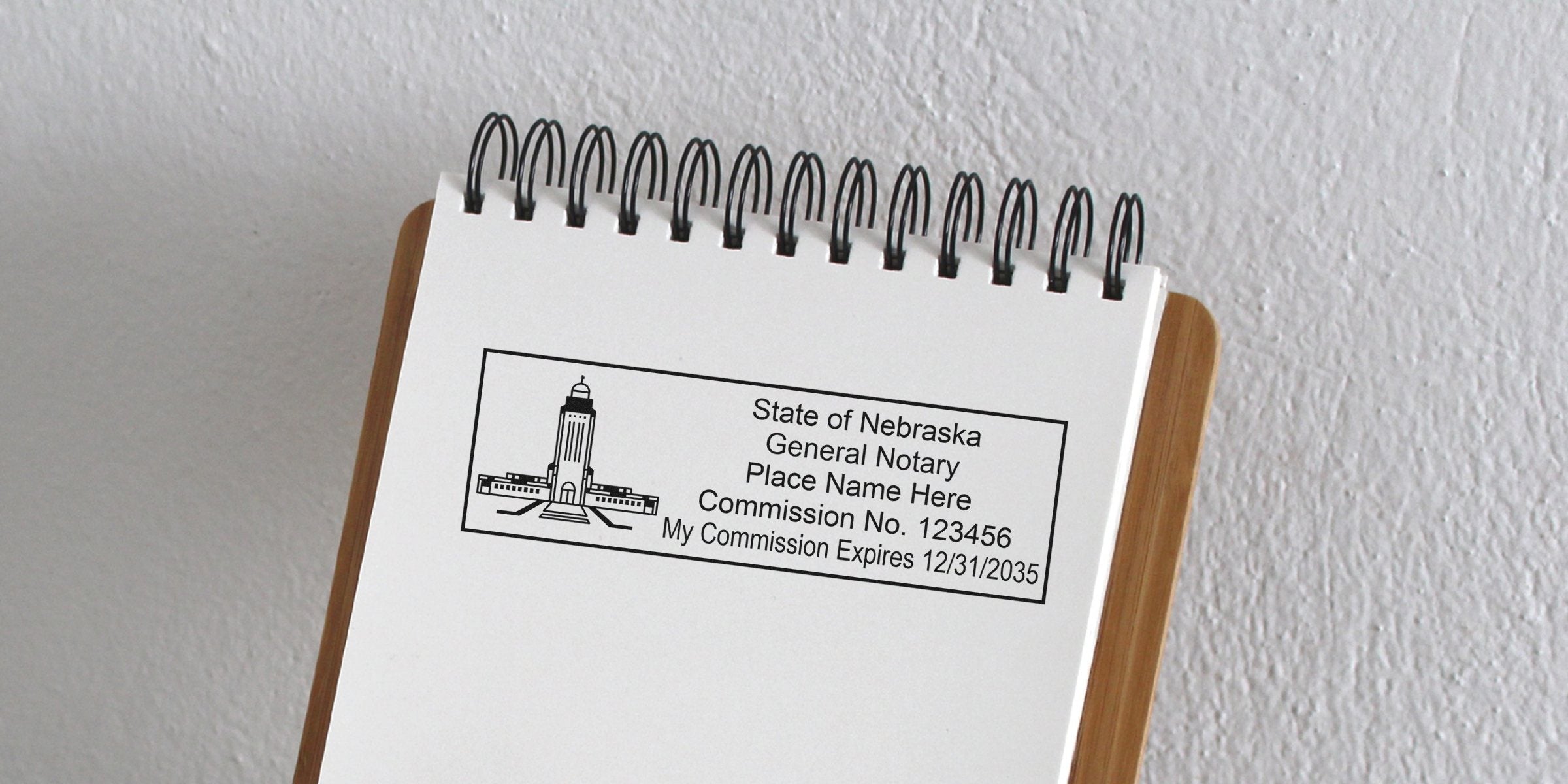 Top view of a spiral notepad showing a Nebraska notary stamp imprint with state capitol graphic, placeholder name, commission number and expiration date on white paper against a textured wall background