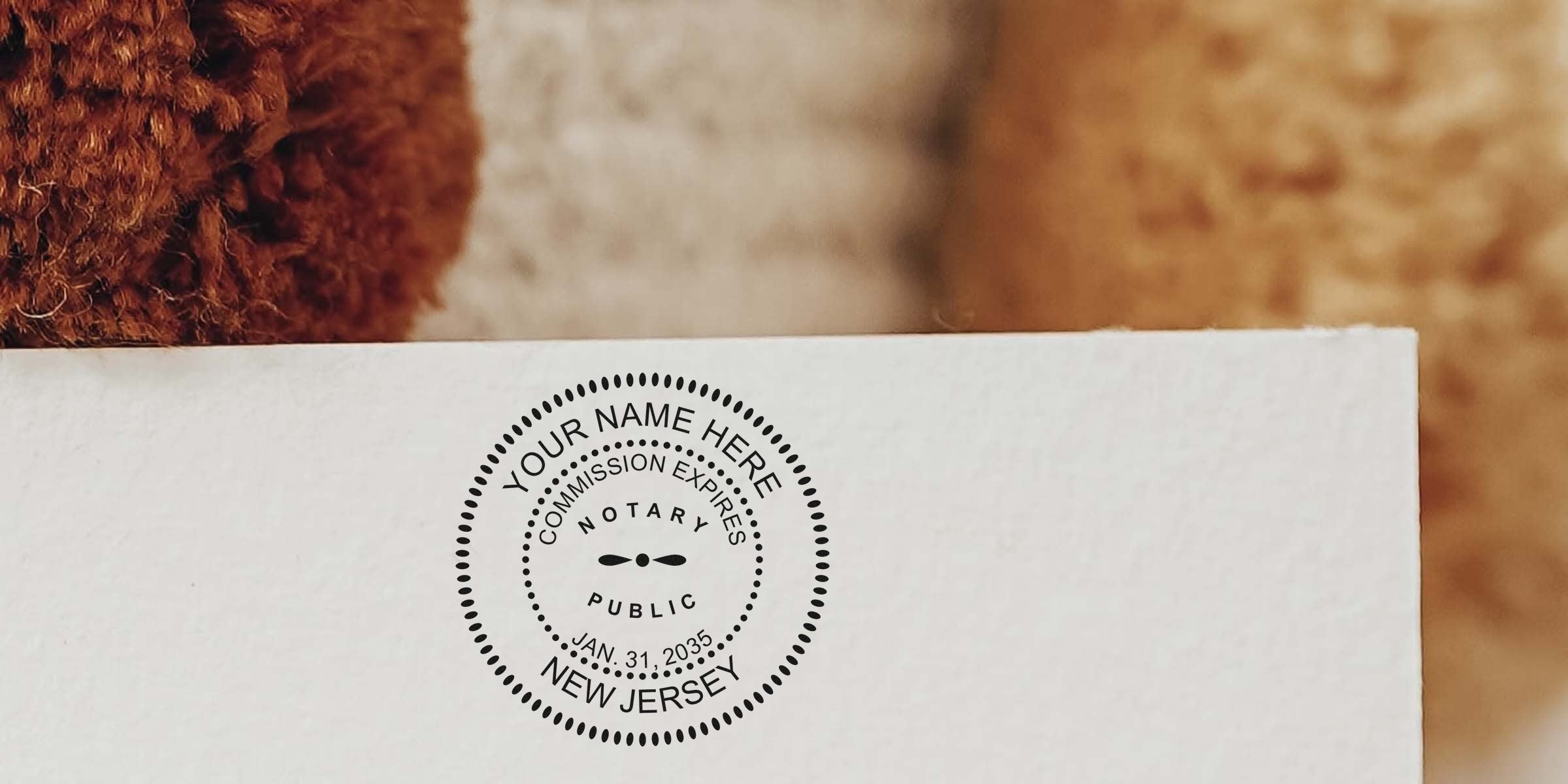 Close-up of a black circular notary public stamp on white paper reading "Notary Public, New Jersey" with commission expiration date, set against a textured brown fabric background