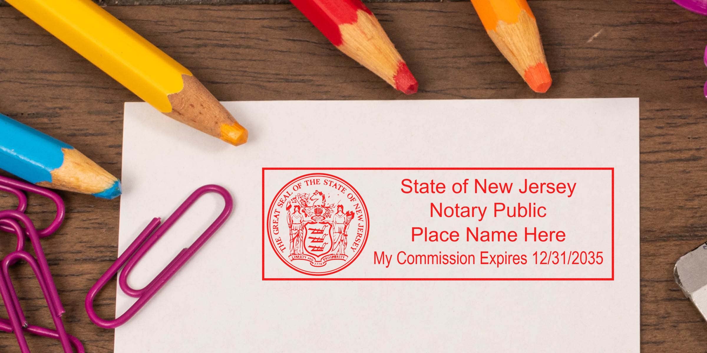 State of New Jersey notary public red stamp on white paper reading "Place Name Here, My Commission Expires 12/31/2035" on a wooden desk with colorful sharpened pencils and purple paperclips nearby.