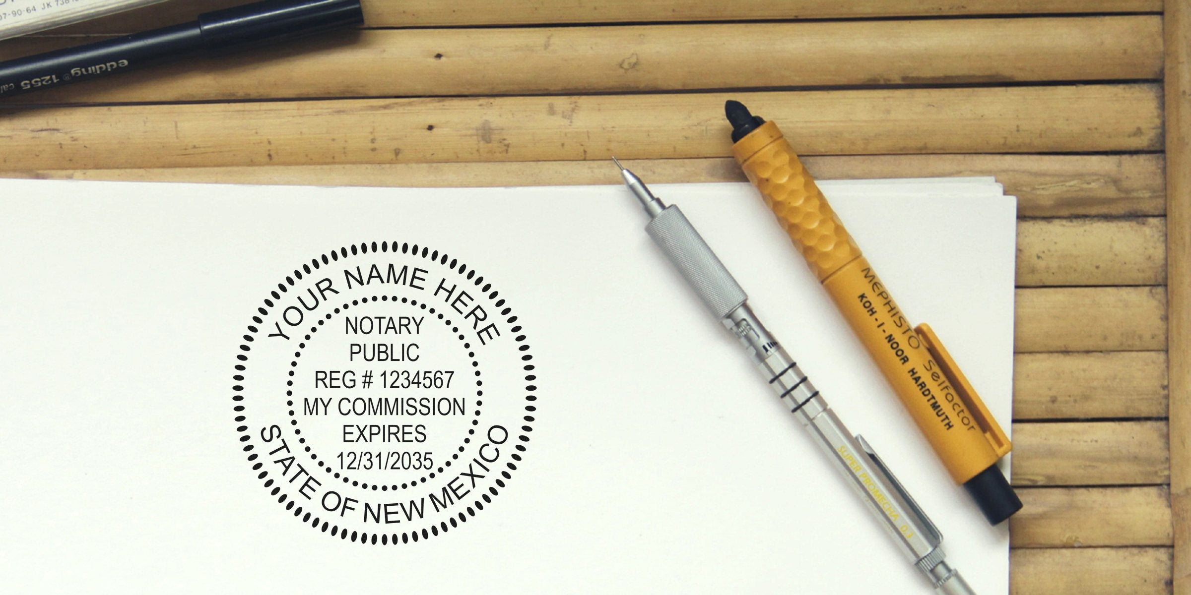 Top-down photo of a notary public circular stamp imprint on white paper reading "Your Name Here, State of New Mexico" with two pens and a mechanical pencil resting on a wooden slatted surface.