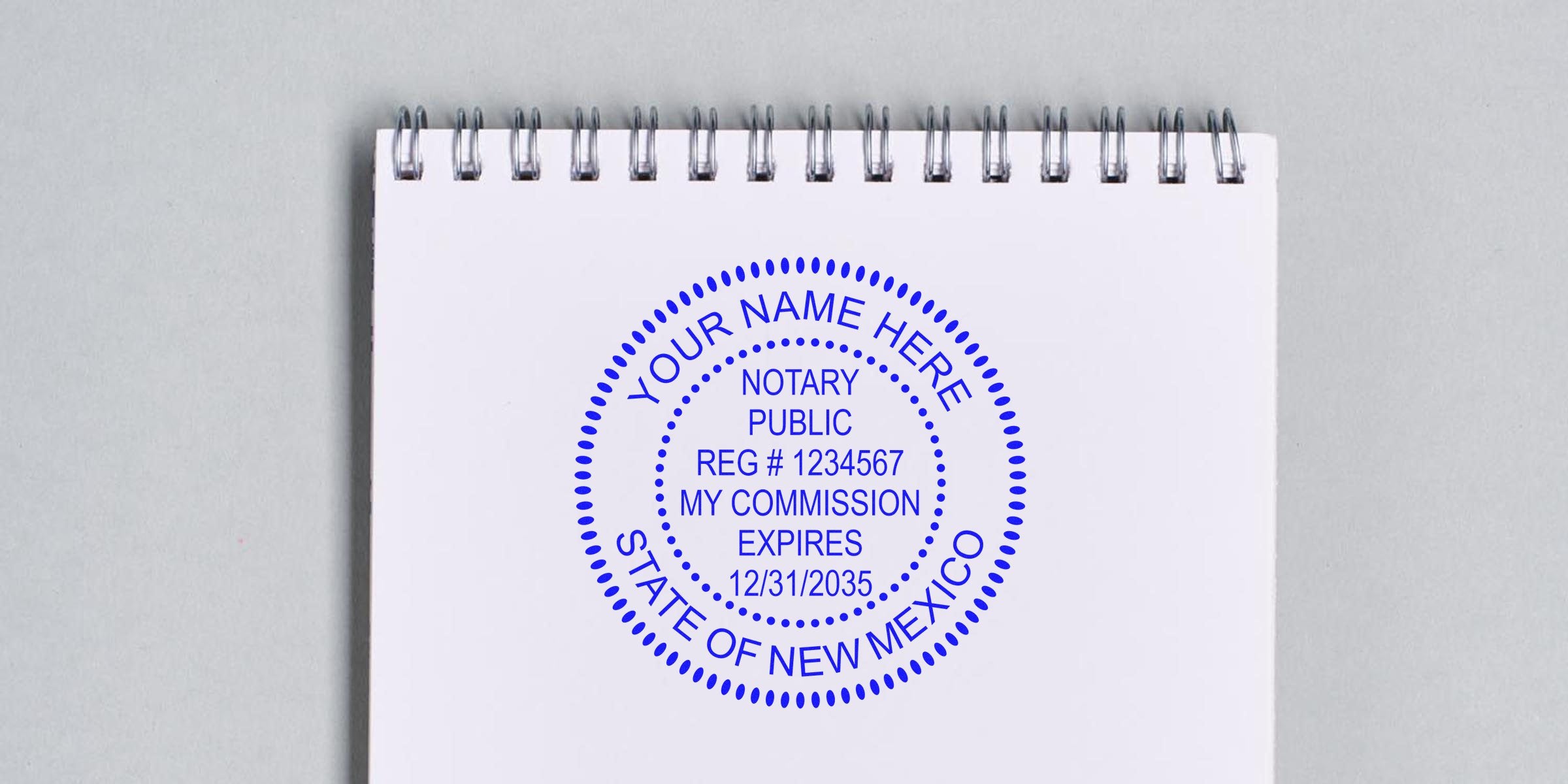 Blue circular notary stamp on a white spiral-bound notepad reading "YOUR NAME HERE, NOTARY PUBLIC, REG # 1234567, MY COMMISSION EXPIRES 12/31/2035, STATE OF NEW MEXICO" on a light gray background.