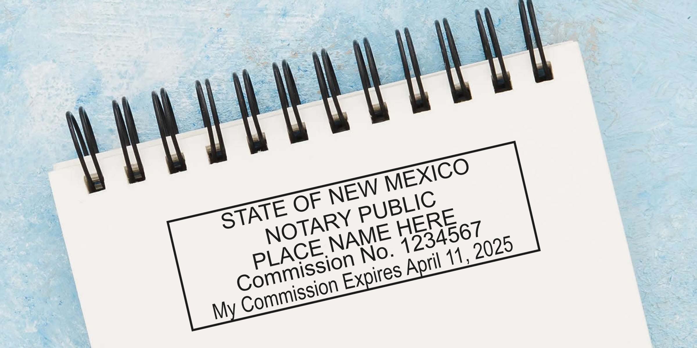 Spiral-bound notebook page with a New Mexico notary public stamp sample showing place for name, commission number and expiration date, black rectangular stamp on white paper against a textured blue background