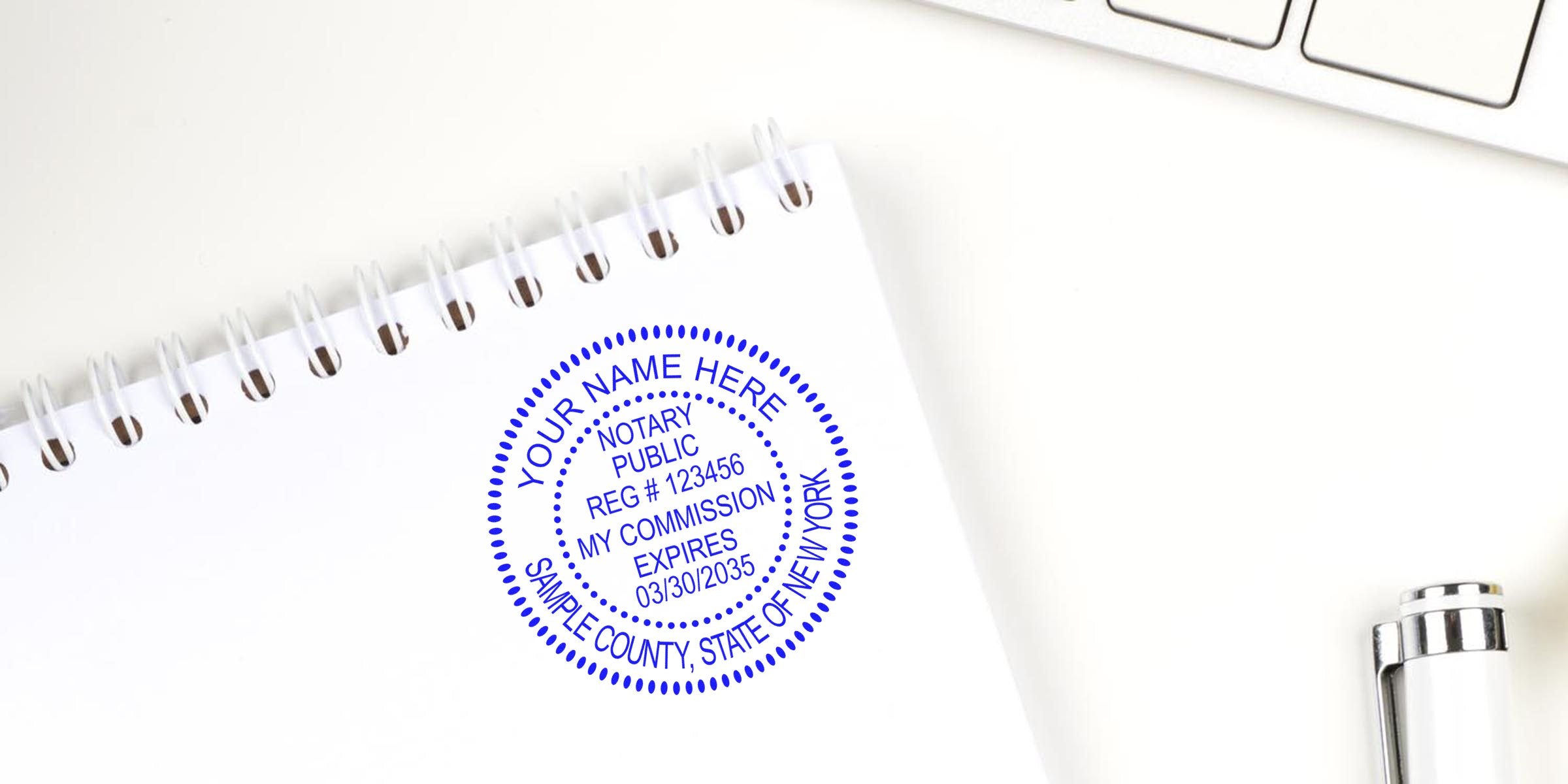 Blue circular notary seal stamped on a white spiral-bound notebook page on a clean white desk, with a partial silver pen and keyboard visible — notary stamp, notary seal, legal document authentication