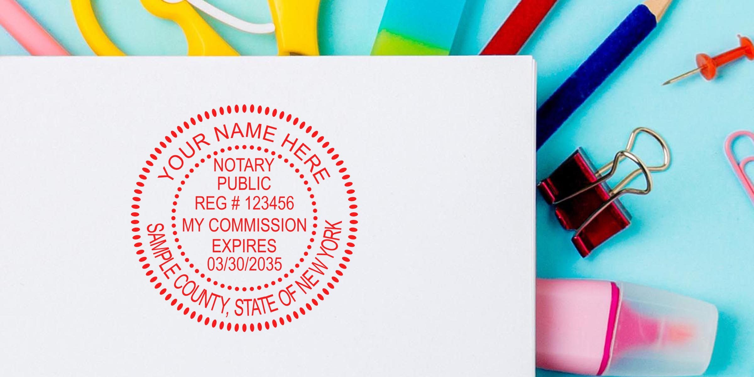 Red notary public stamp imprint on white paper reading "Notary Public" and sample county/state text, surrounded by colorful office supplies (binder clip, push pin, highlighter) on a bright blue background