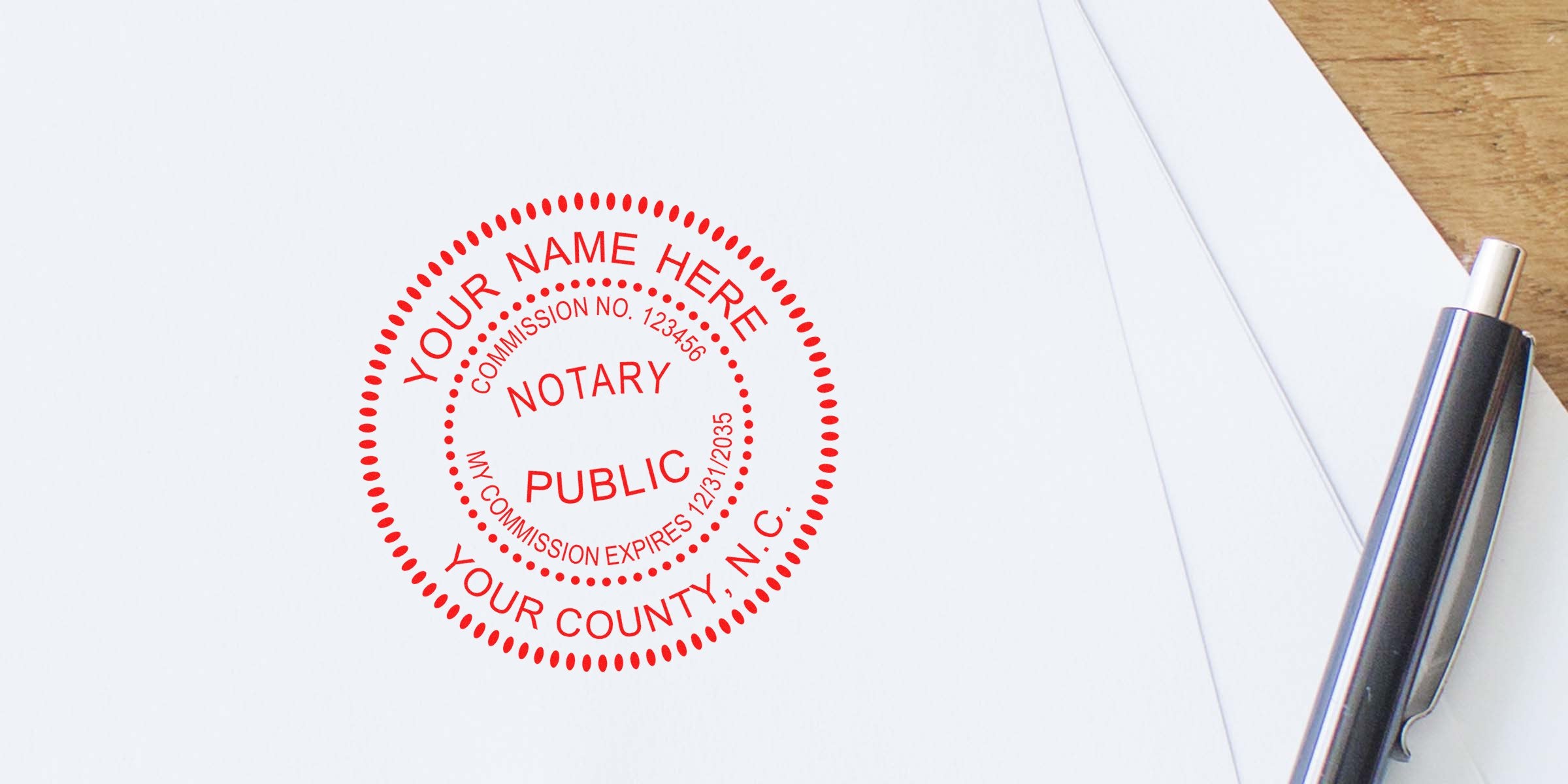 Red circular notary public stamp on white paper beside a silver pen, customizable "Your Name Here" text with commission number and expiration date visible — notary seal for legal documents, notarization services, and stationery branding