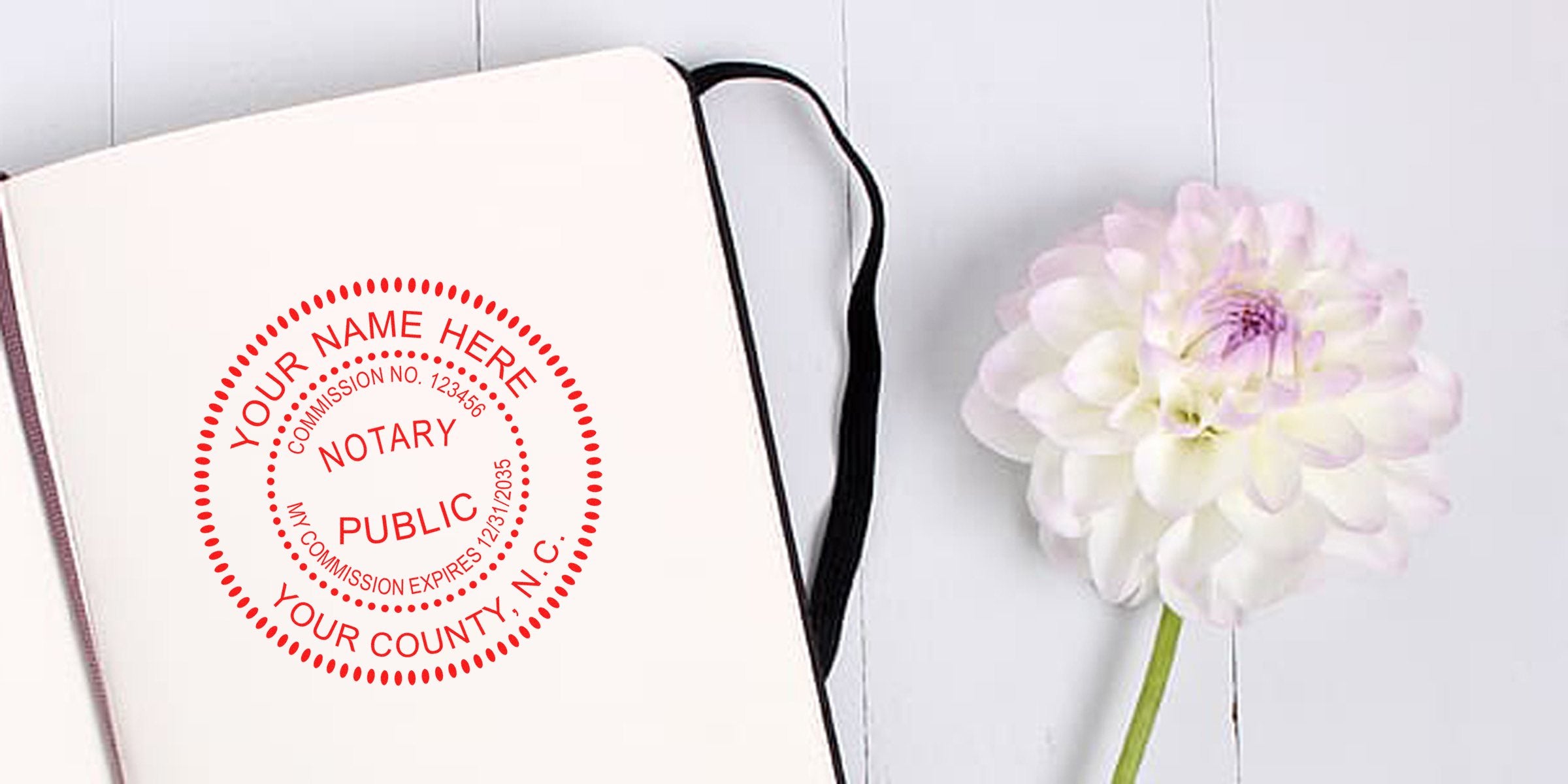 Open notebook with red circular notary public stamp mockup on blank page beside pale pink dahlia on white wooden background — stationery, notary seal, floral desk flat lay for branding or office decor