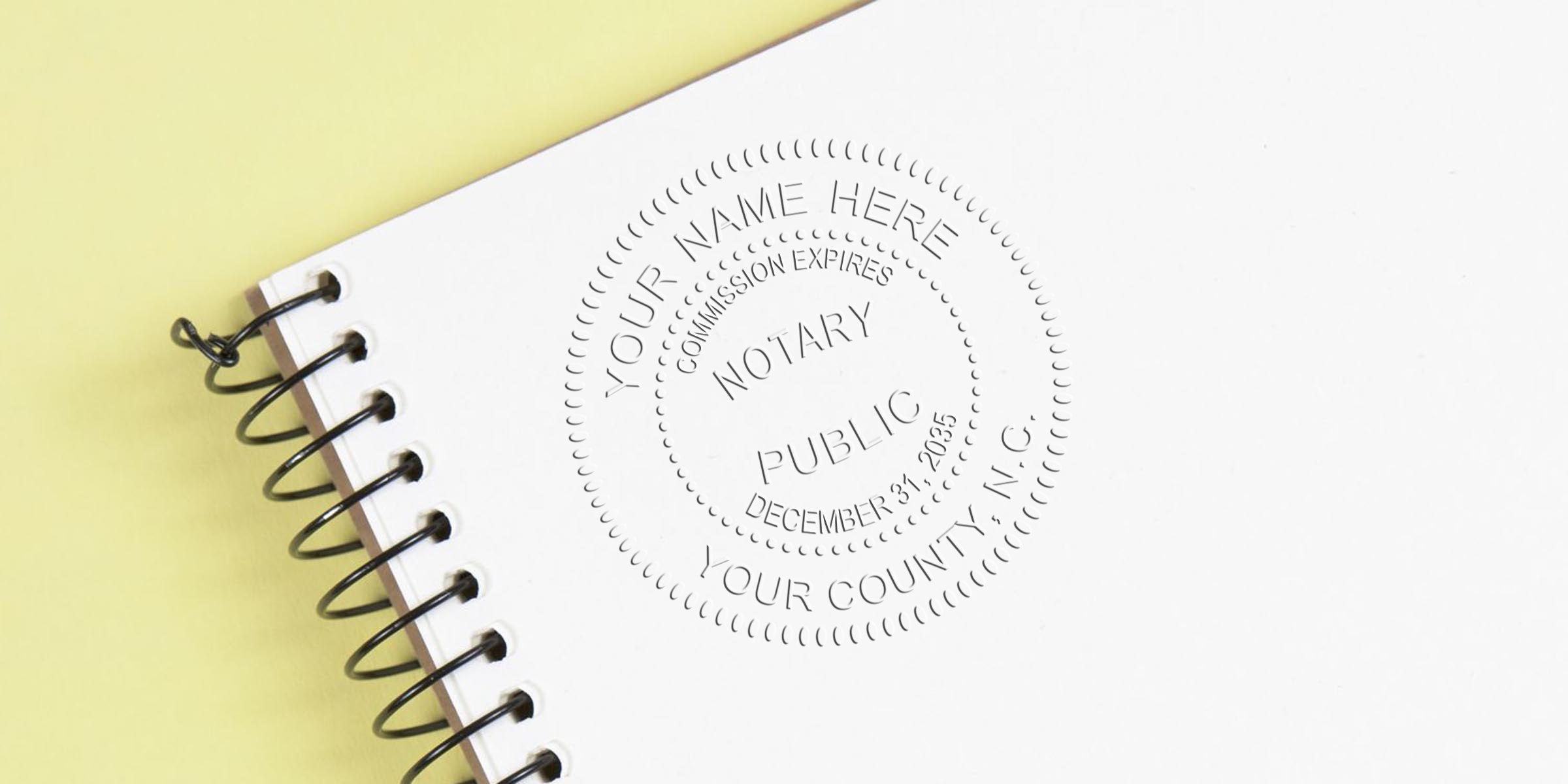 Spiral-bound notebook on pale yellow background with an embossed notary public seal stamped into white paper reading "Your Name Here," "Notary Public," and expiration details.