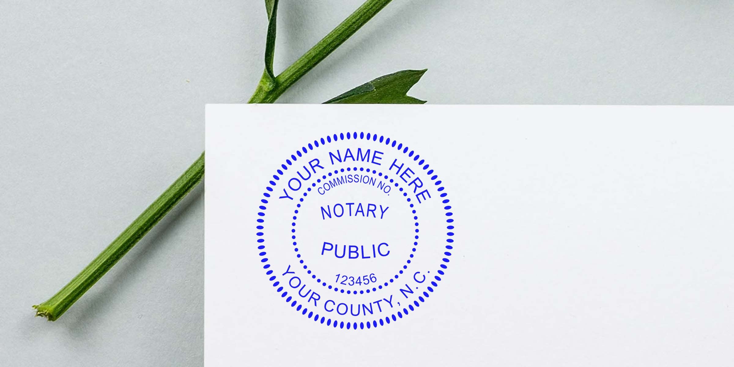 Blue circular notary public stamp on white paper with dotted border and sample text "Your Name Here, Your County, NC, Commission No. 123456", green plant stem background