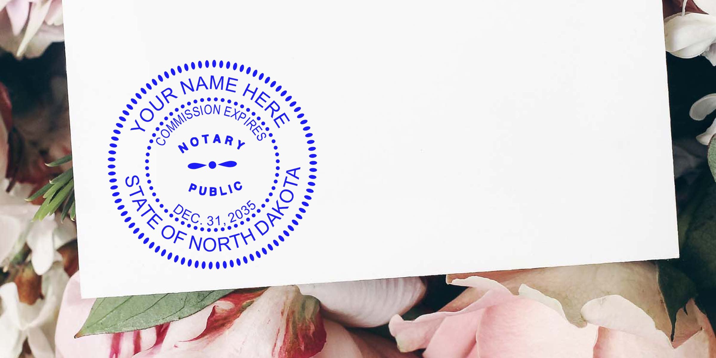 Blue circular notary public stamp reading "Your Name Here" and "State of North Dakota" on a white card placed over pink peony flowers.