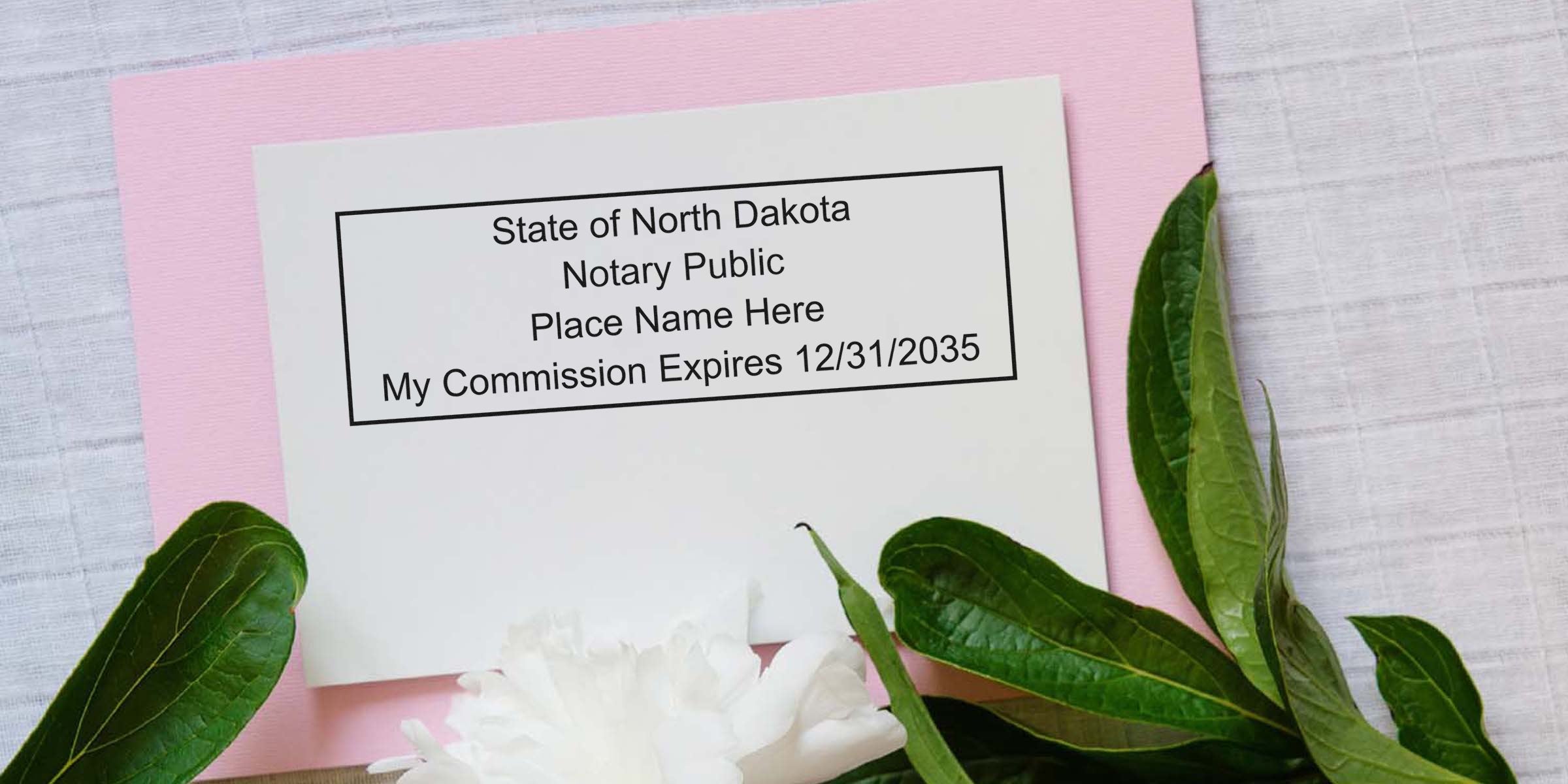 White notary sample card reading "State of North Dakota Notary Public Place Name Here My Commission Expires 12/31/2035" on pink paper with green leaves and white peony on fabric background
