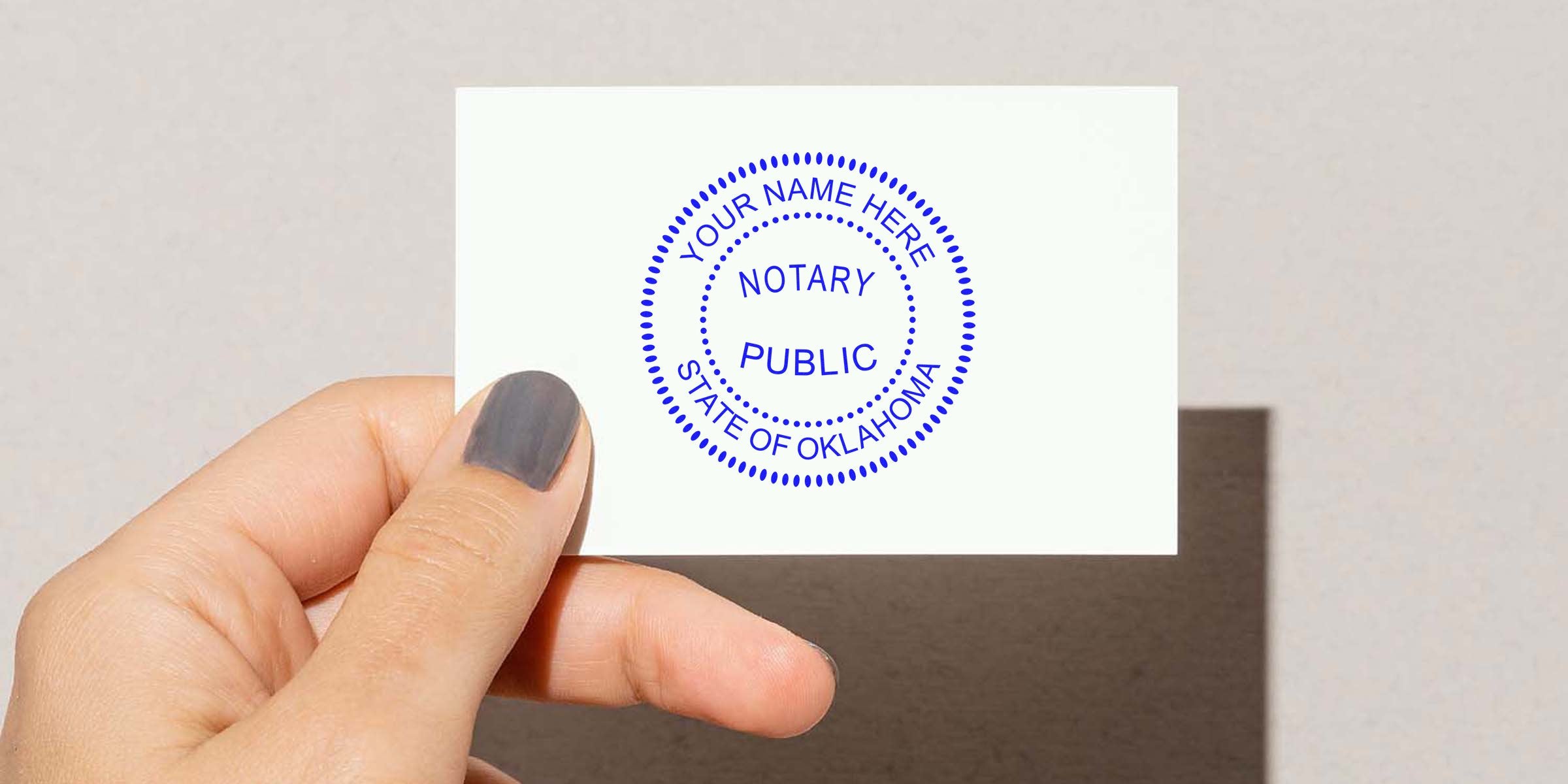 Hand holding a white card with a blue circular Notary Public stamp reading "Your Name Here" and "State of Oklahoma" — notary public stamp business card mockup