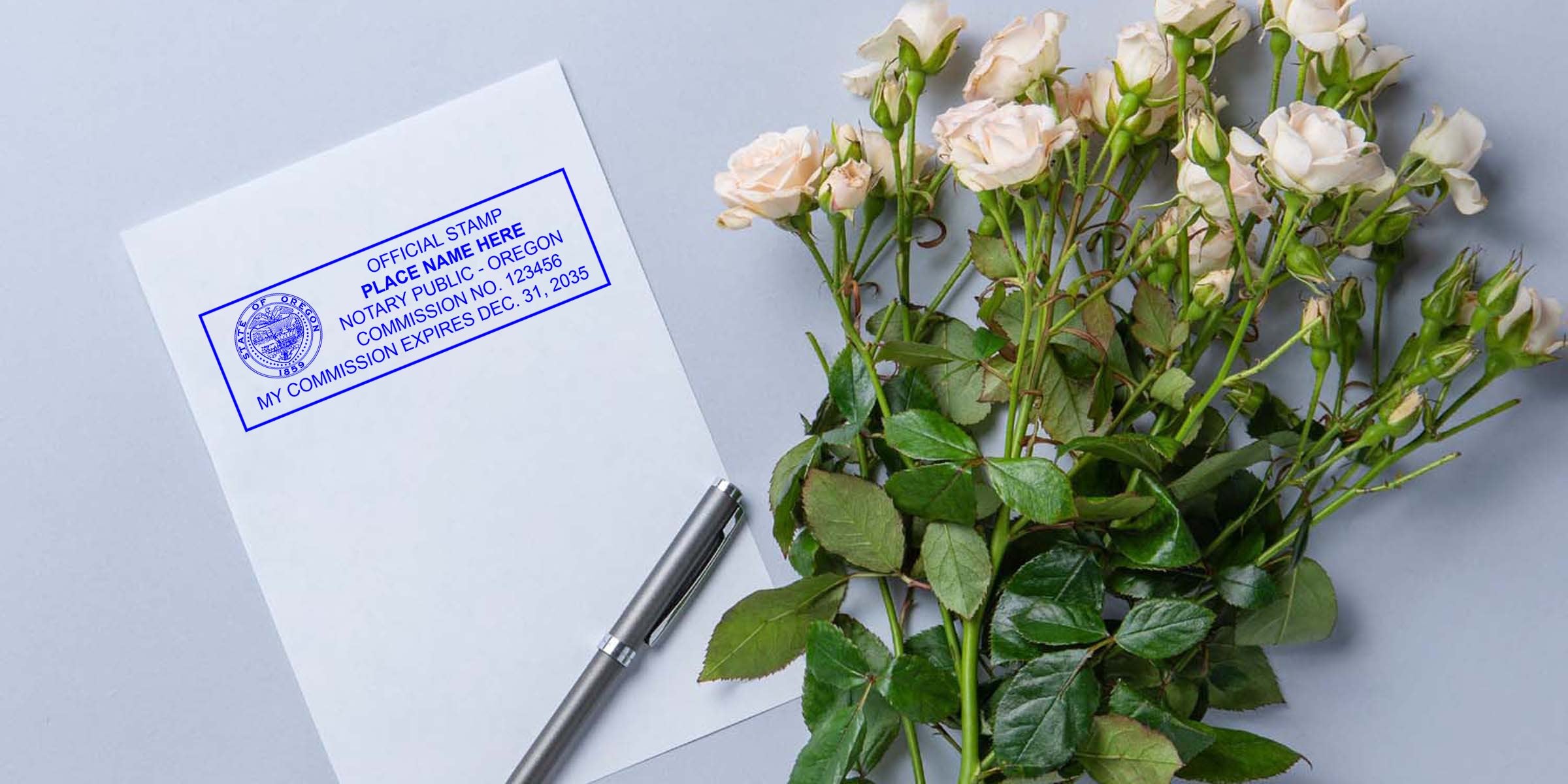Notary stamp on white document beside a silver pen and pale pink rose bouquet on a gray background — official notary public stamp, commission details, stationery and floral arrangement for legal document or wedding paperwork visuals