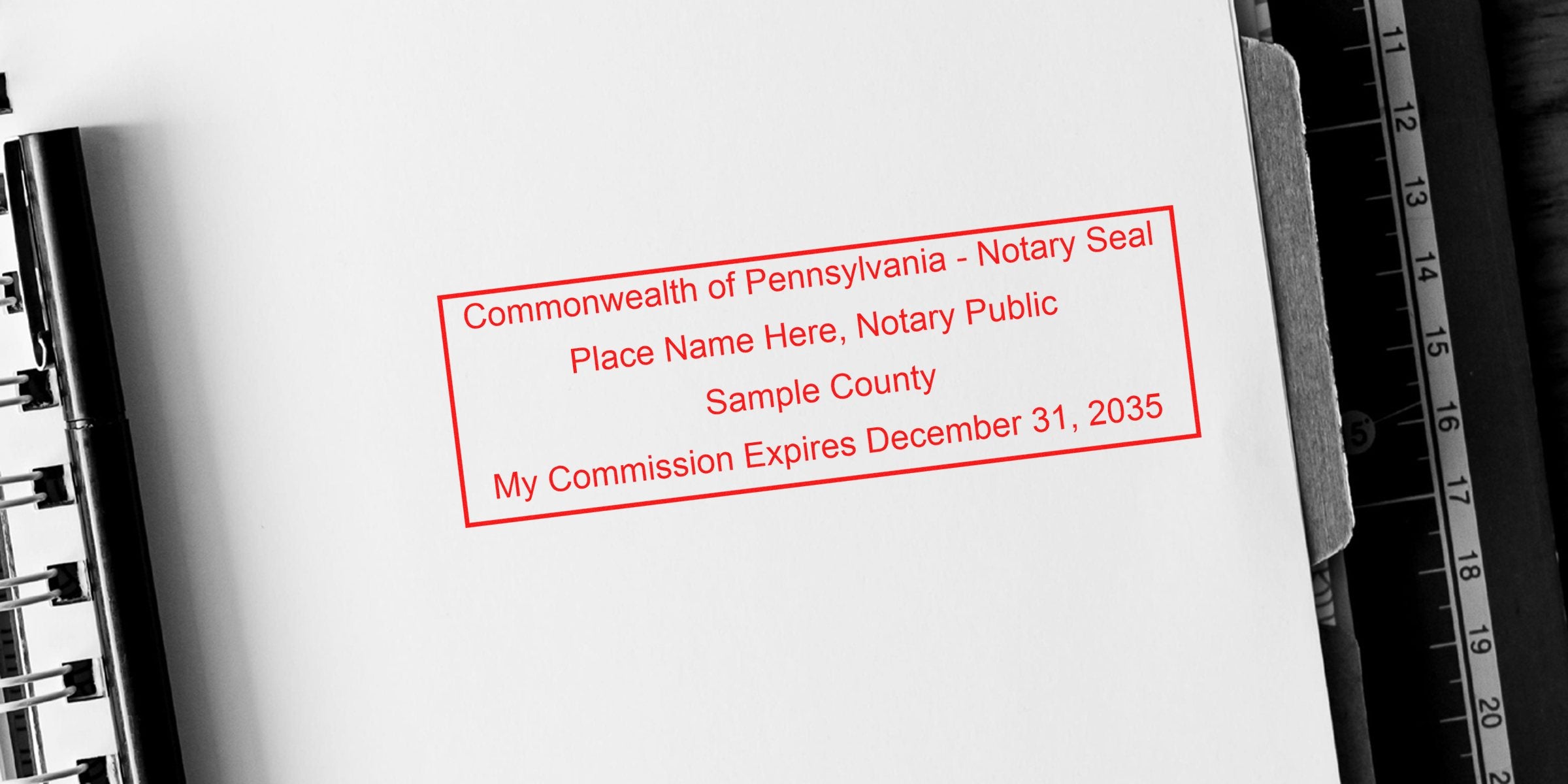 Red rectangular notary seal stamp on white paper reading "Commonwealth of Pennsylvania - Notary Seal; Place Name Here, Notary Public; Sample County; My Commission Expires December 31, 2035" beside a spiral notebook and ruler.