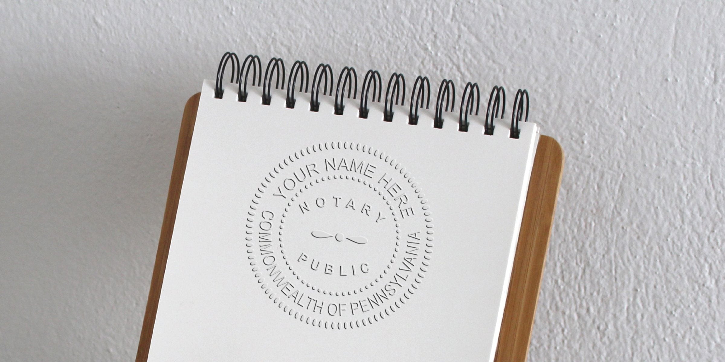 Close-up of a spiral-bound clipboard with an embossed notary public seal on white paper reading "Notary Public, Commonwealth of Pennsylvania"