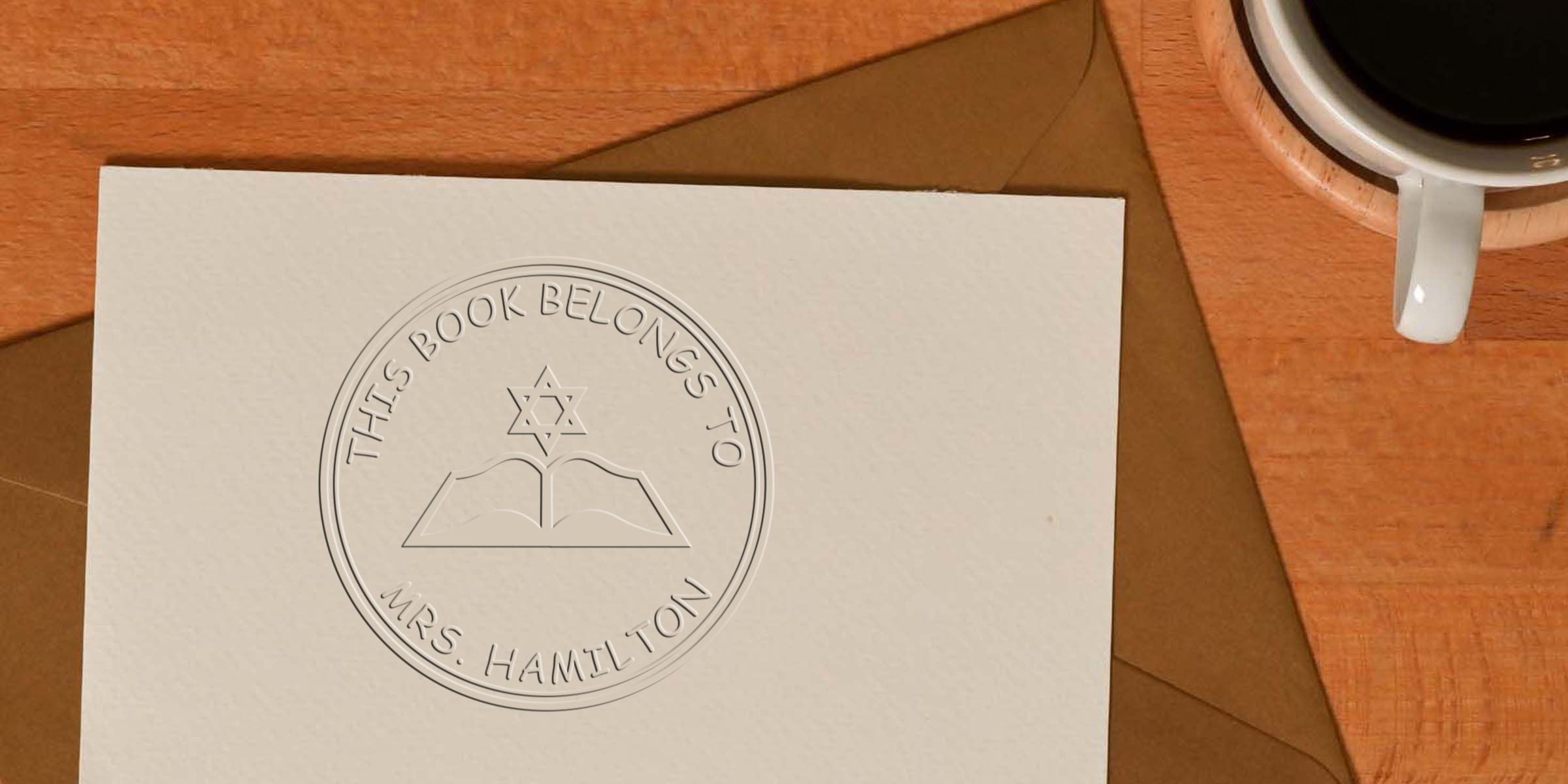 Card with an embossed circular seal that reads “This Book Belongs To Mrs. Hamilton,” featuring a Star of David above an open book.