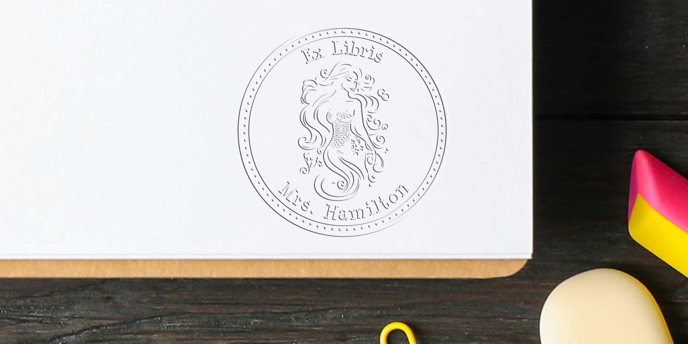 A line drawing of a mermaid inside a circular coin with a dotted border and the text “Ms Hamilton” at the bottom.