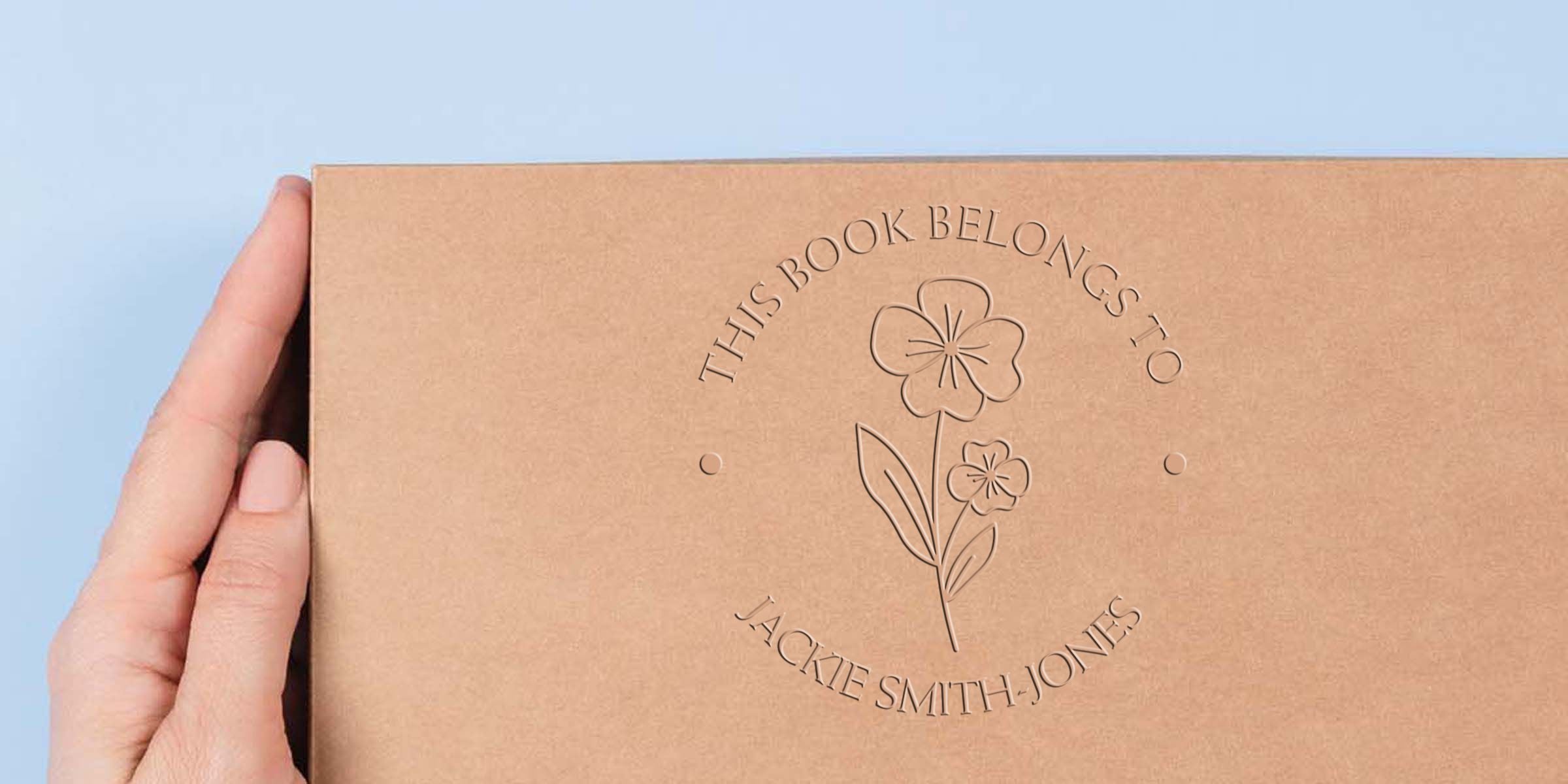 Cardboard box with embossed flower design and circular text reading “This book belongs to Jackie Smith Jones.”