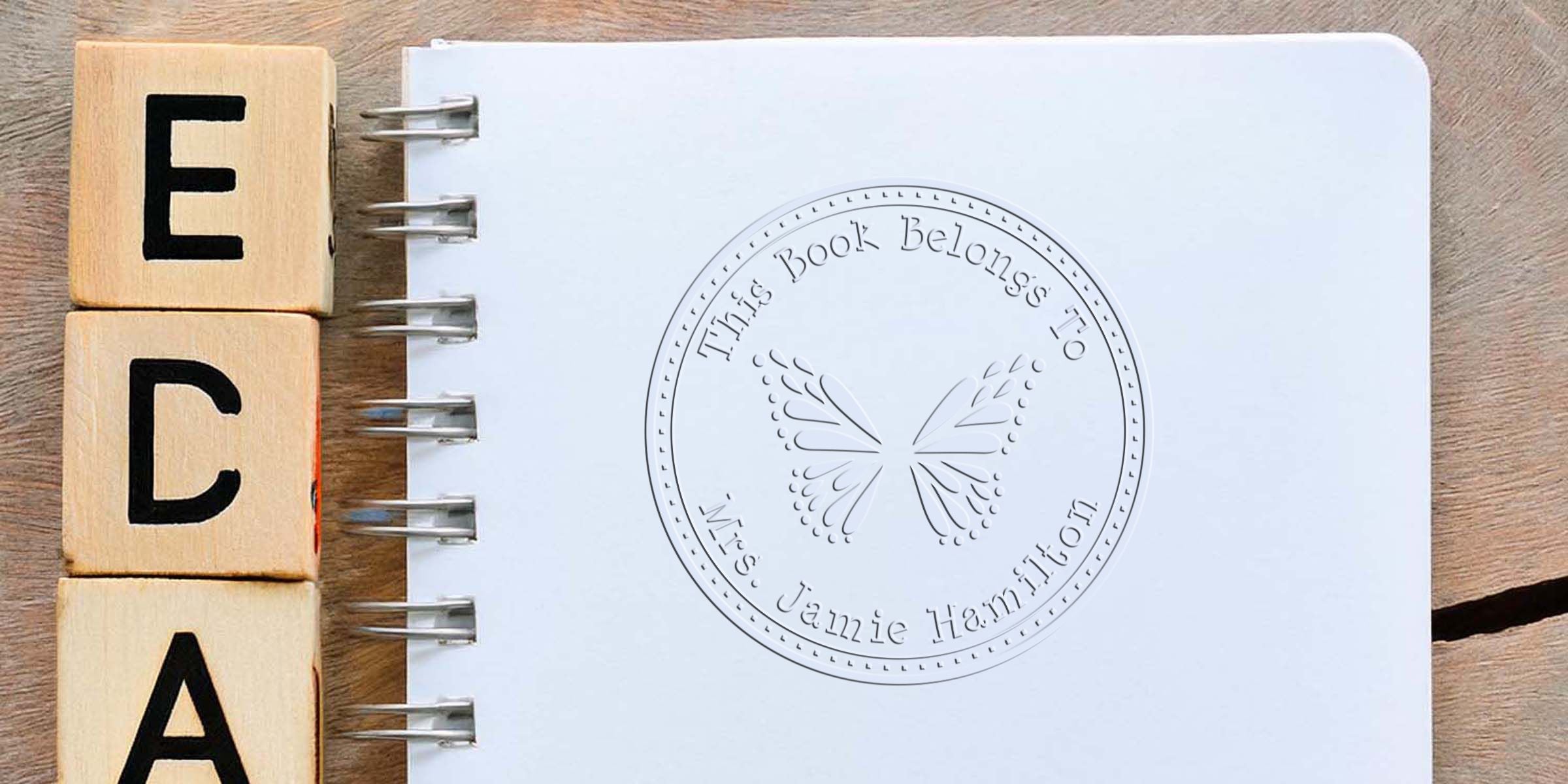 Three wooden blocks spell “ECA” beside a spiral notebook with a circular butterfly logo.