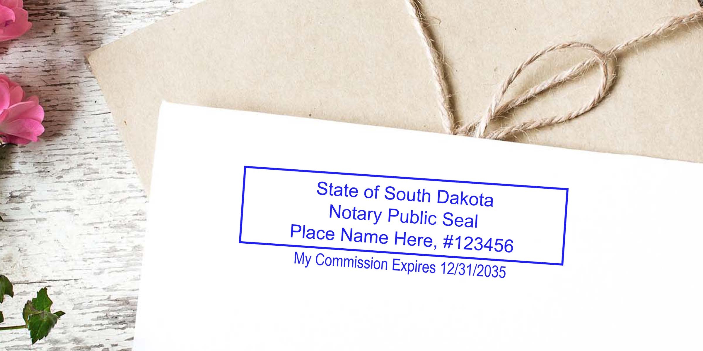 Envelope with blue "State of South Dakota Notary Public Seal" rectangular stamp (placeholder name & commission expiration), kraft paper package with twine, pink flowers on rustic white wood background
