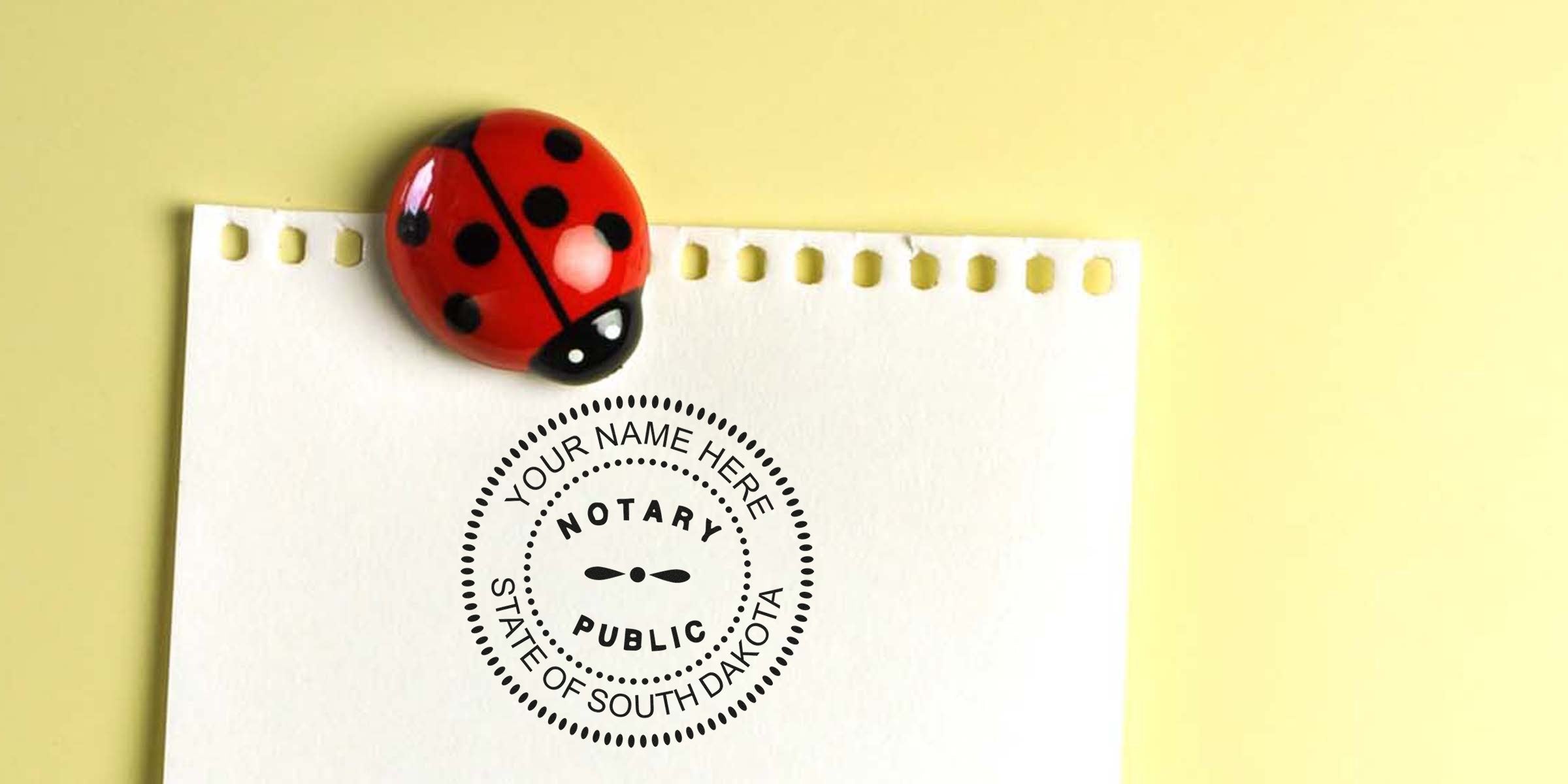 Red ladybug magnet clipping a torn-edge white notepad page stamped with a circular "Notary Public, State of South Dakota" seal on a pale yellow background