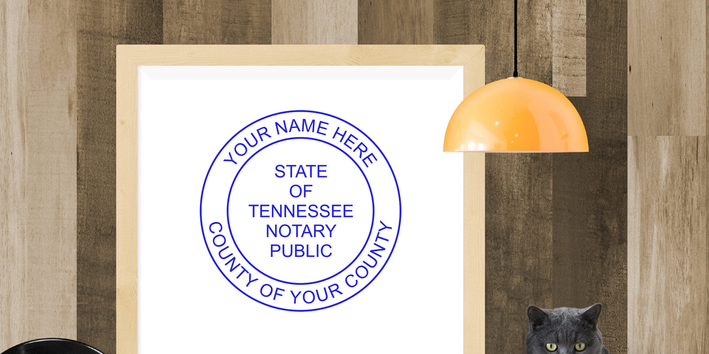 Framed mockup of Tennessee notary public seal in blue on white, mounted on wood plank wall with orange pendant lamp and gray cat.