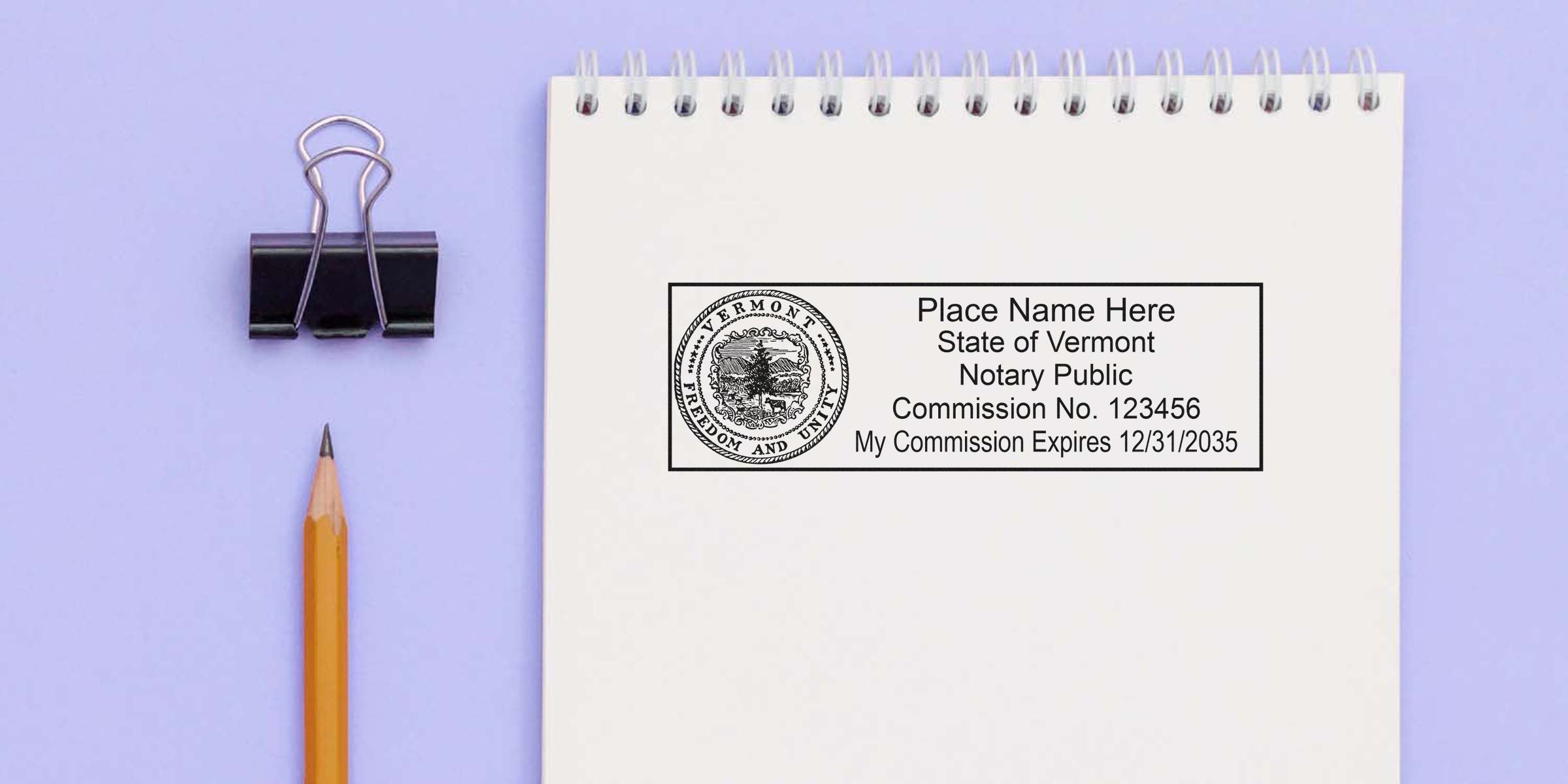 Spiral notebook page showing a Vermont notary public stamp template and seal mockup, with pencil and binder clip on lavender background