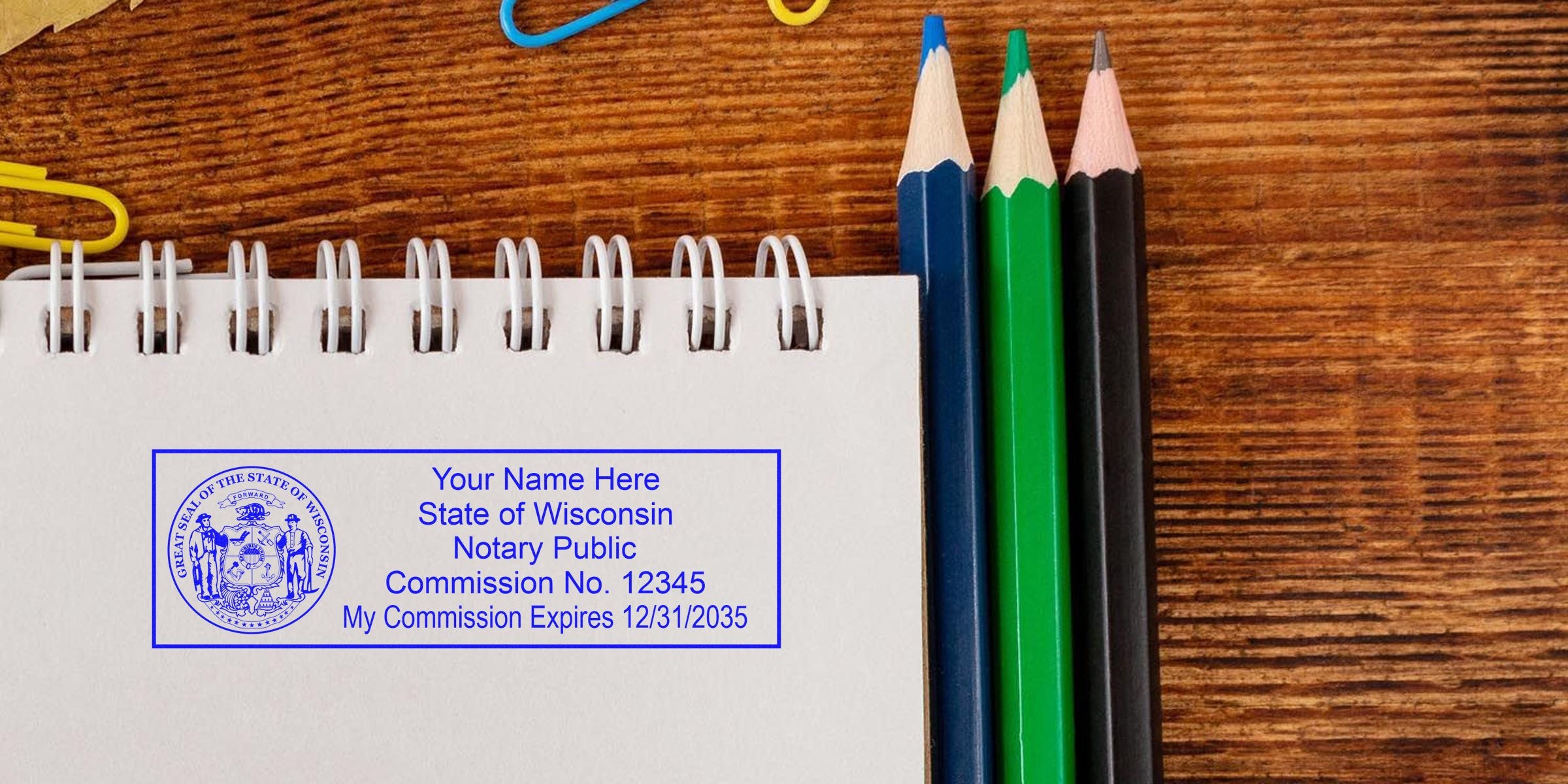 Spiral notebook with blue Wisconsin notary public stamp sample on paper beside green, blue and black colored pencils on wooden desk — notary stamp mockup, office stationery image