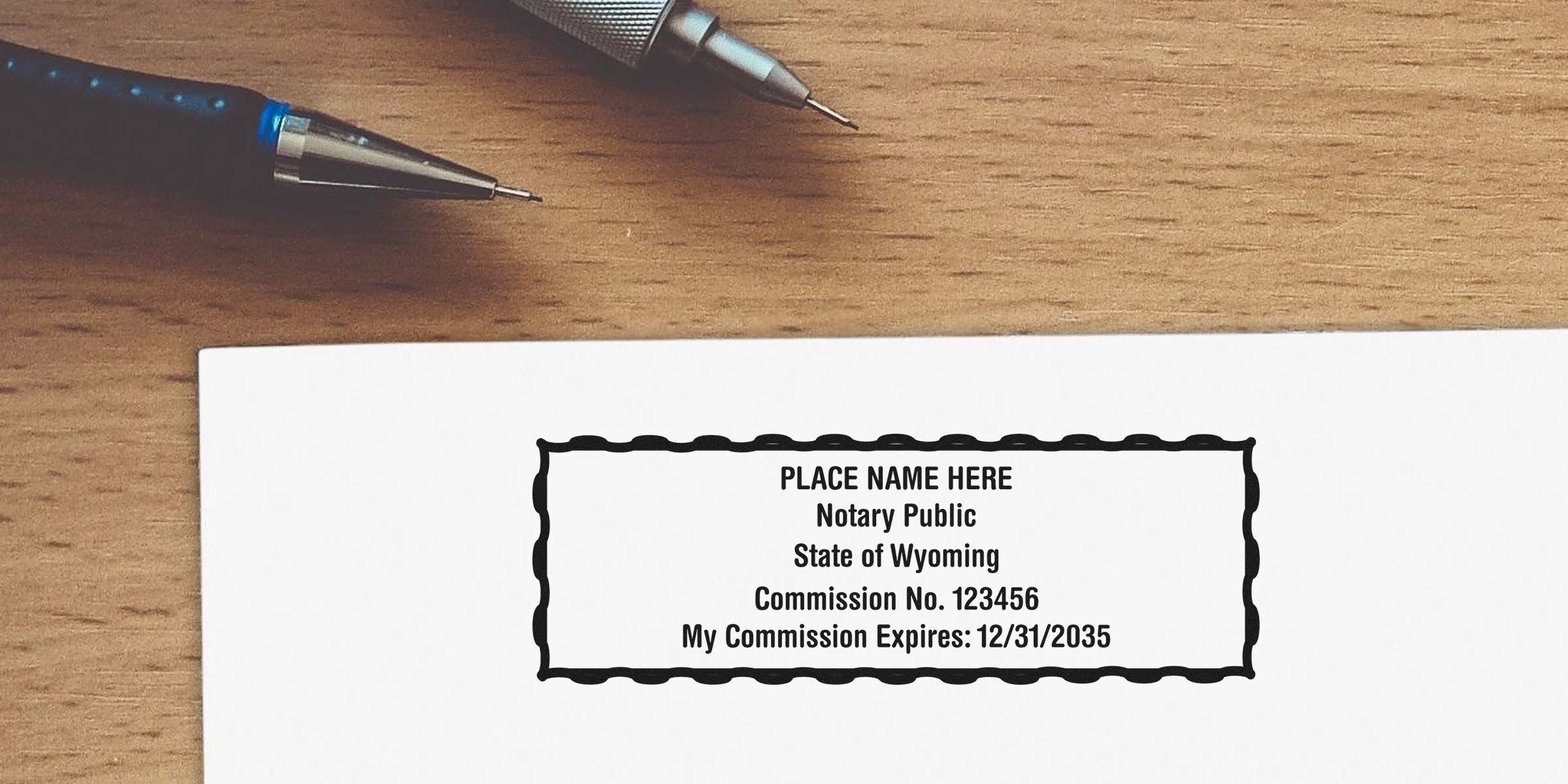 Top-down view of a notary public stamp imprint on white paper reading "Notary Public State of Wyoming Commission No. 123456 Expires 12/31/2035" with two mechanical pencils on a wooden desk.