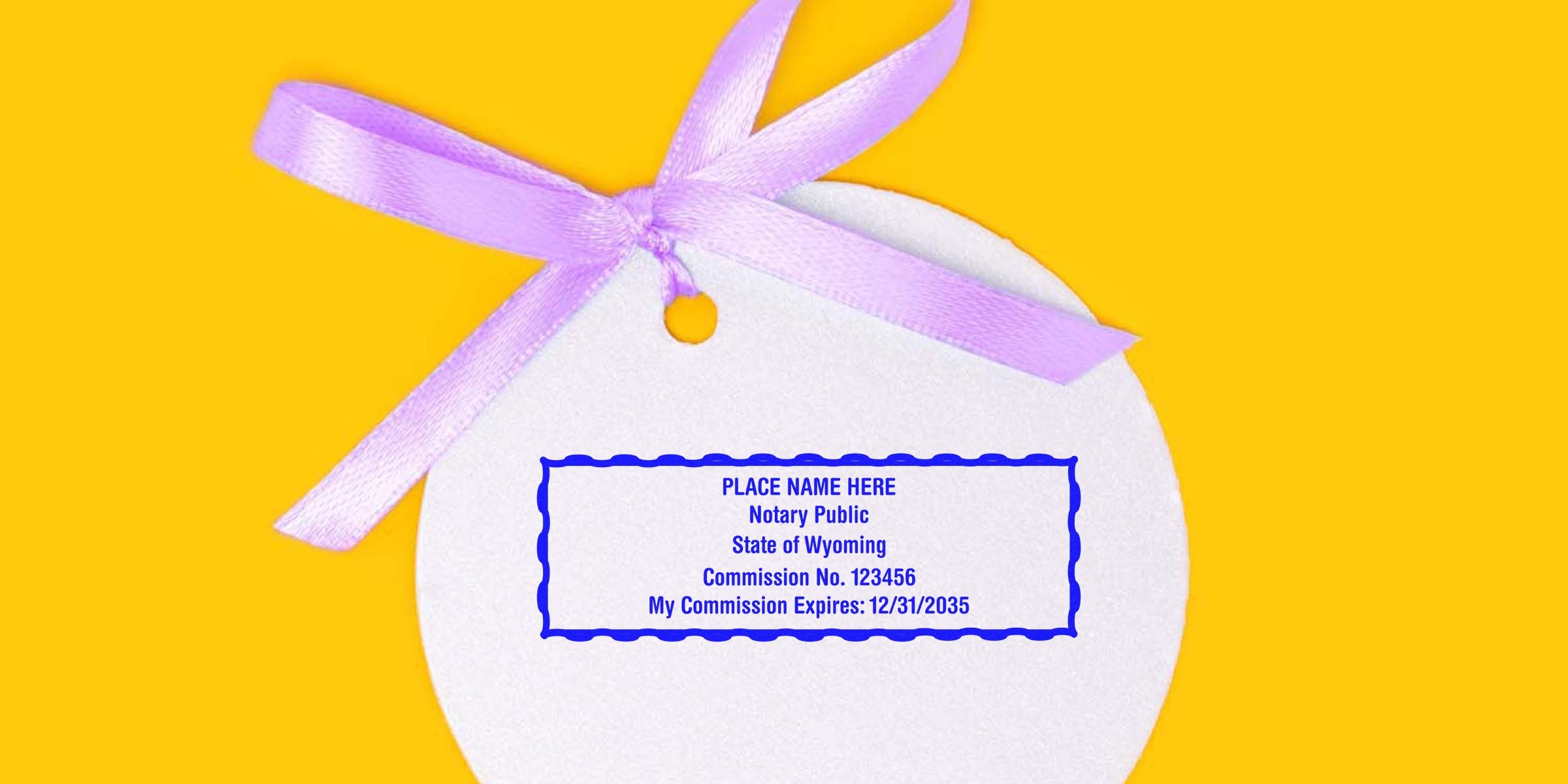 Round white gift tag with purple ribbon on yellow background featuring a blue notary public stamp mockup reading "Place Name Here, State of Wyoming, Commission No. 123456, Expires 12/31/2035"