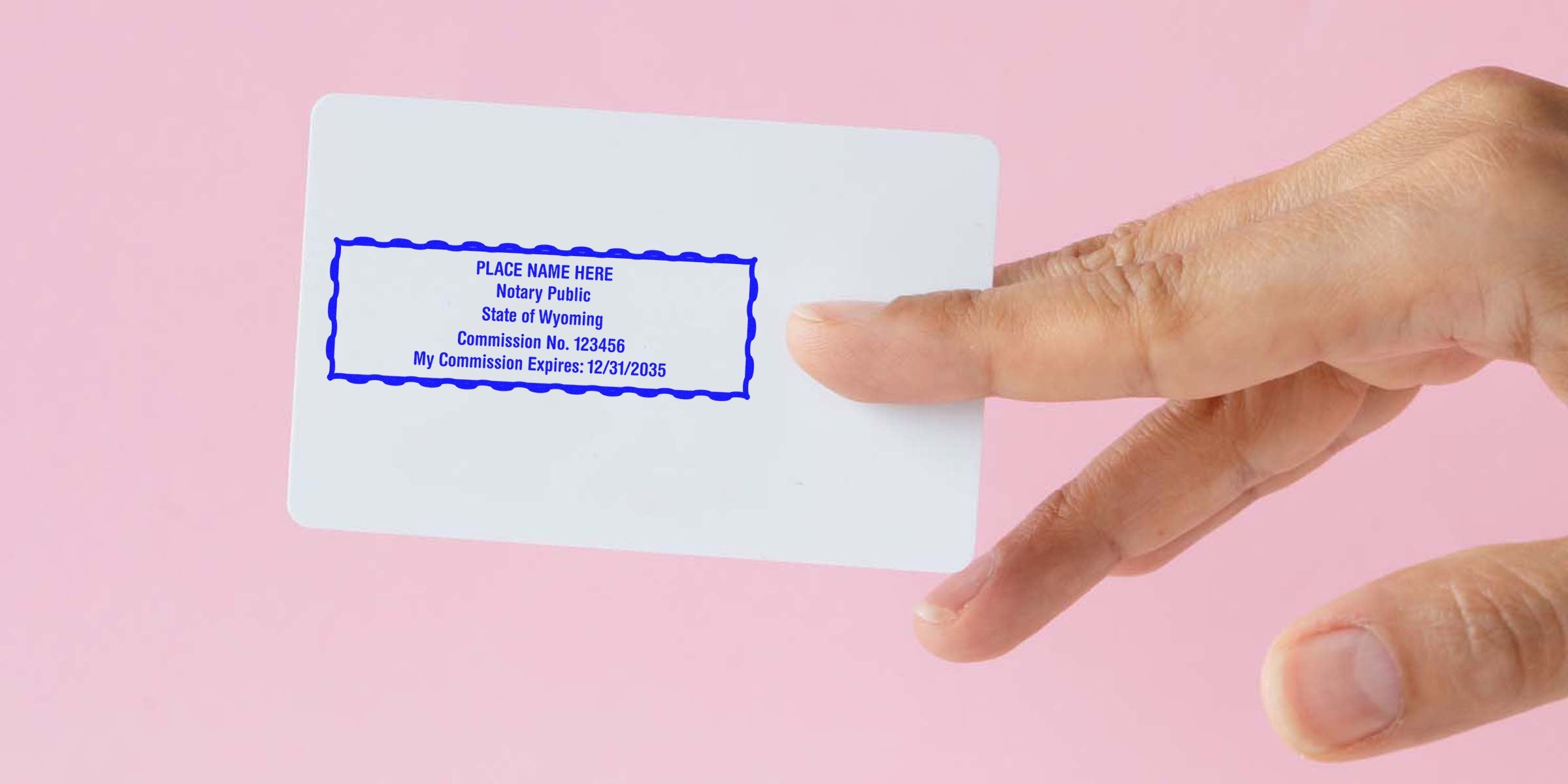 Hand holding white card with blue notary public stamp showing commission number and expiration date on pink background
