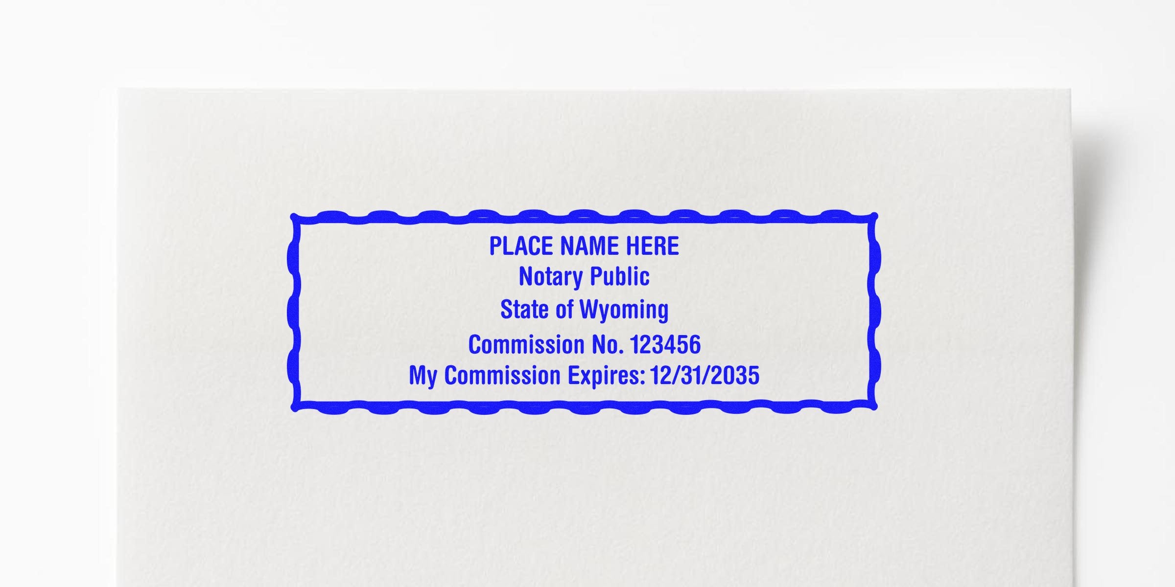 Blue rectangular notary stamp mockup on white paper reading "PLACE NAME HERE Notary Public State of Wyoming Commission No. 123456 My Commission Expires: 12/31/2035" with scalloped border.