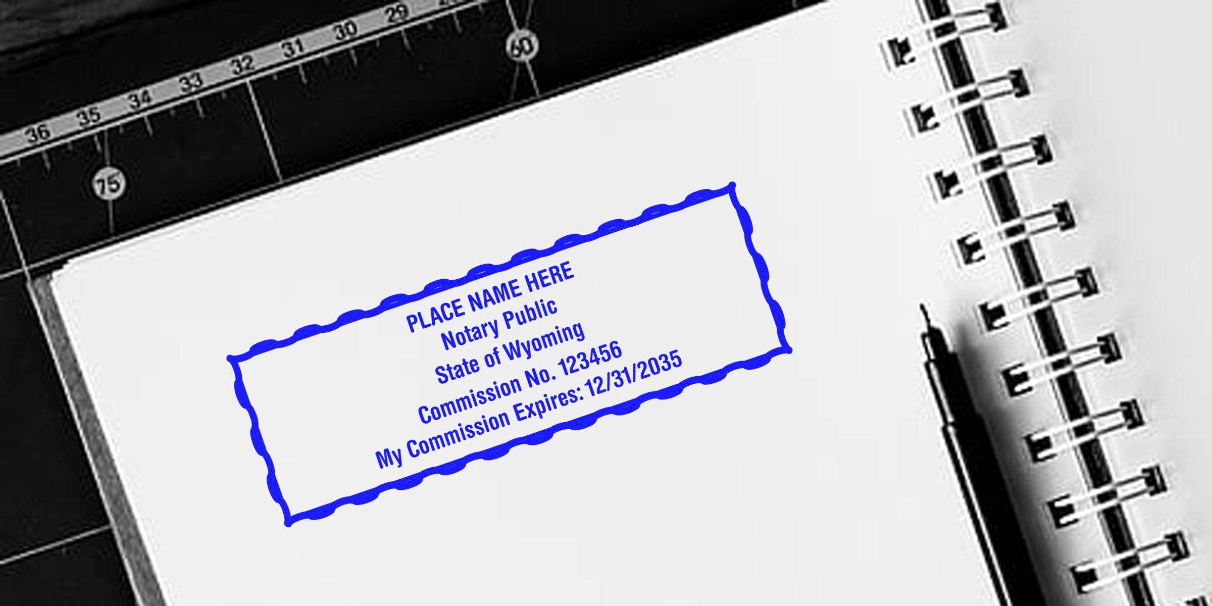 Blue rectangular notary stamp reading "Notary Public State of Wyoming Commission No. 123456 My Commission Expires 12/31/2035" on a white spiral notebook page with a black pen and cutting mat.