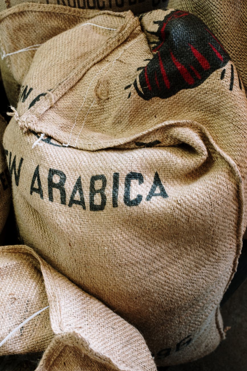 Stacked burlap sacks labeled "Arabica" for coffee, close-up showing coarse texture, stitching and printed coffee bean logo—raw coffee bean storage, wholesale coffee supply imagery
