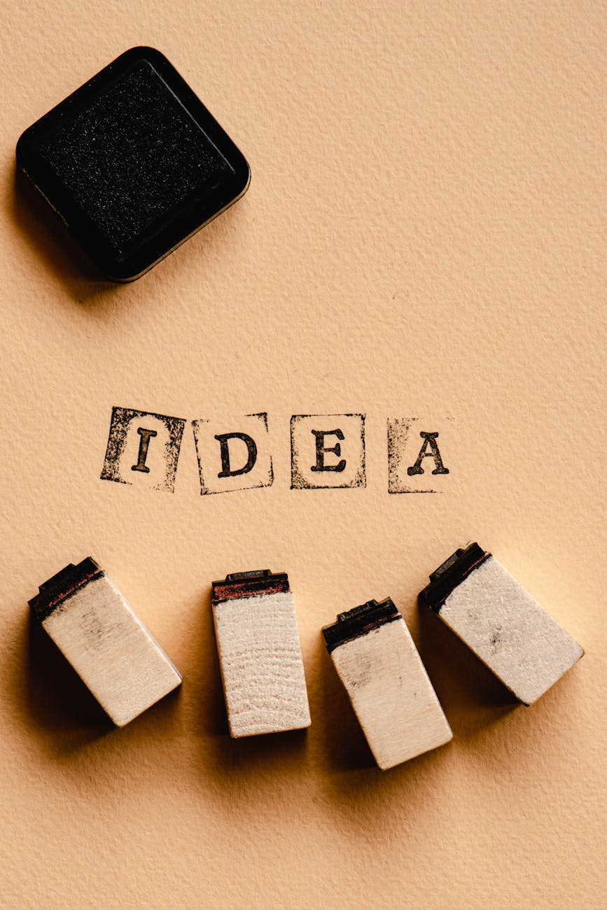 Top view of a black ink pad and four wooden rubber stamp blocks on beige paper with the word "IDEA" stamped in vintage square letters — creative concept, brainstorming, office supplies.
