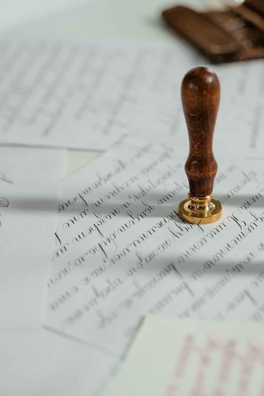 Wooden-handle brass wax seal stamp resting on elegant calligraphy handwritten letters and vintage stationery envelopes.