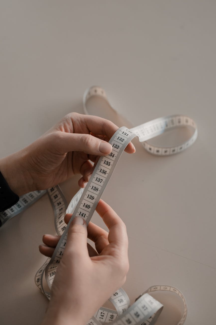 Close-up of hands holding a white measuring tape with visible centimeter numbers, tailoring and sewing measurement concept.
