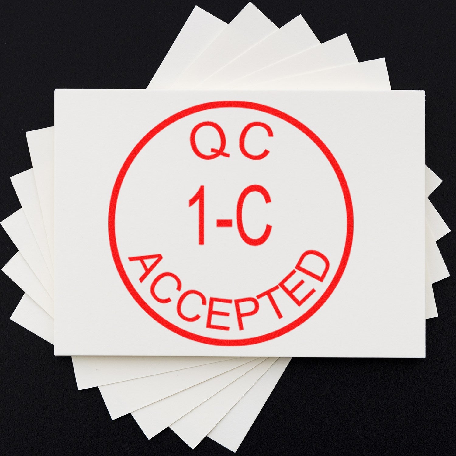 Red QC 1-C ACCEPTED stamp and seal on stacked white cards against a black background