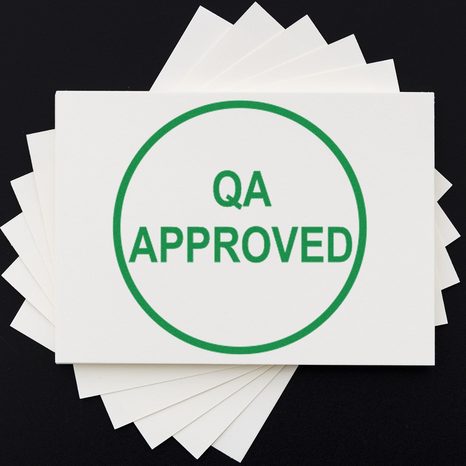 Green circular QA APPROVED stamp seal on stacked white cards against a black background