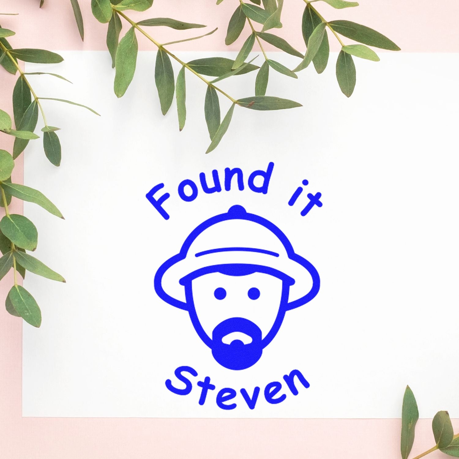 Blue custom stamp seal reading Found it Steven with face icon on white paper, framed by green eucalyptus leaves.