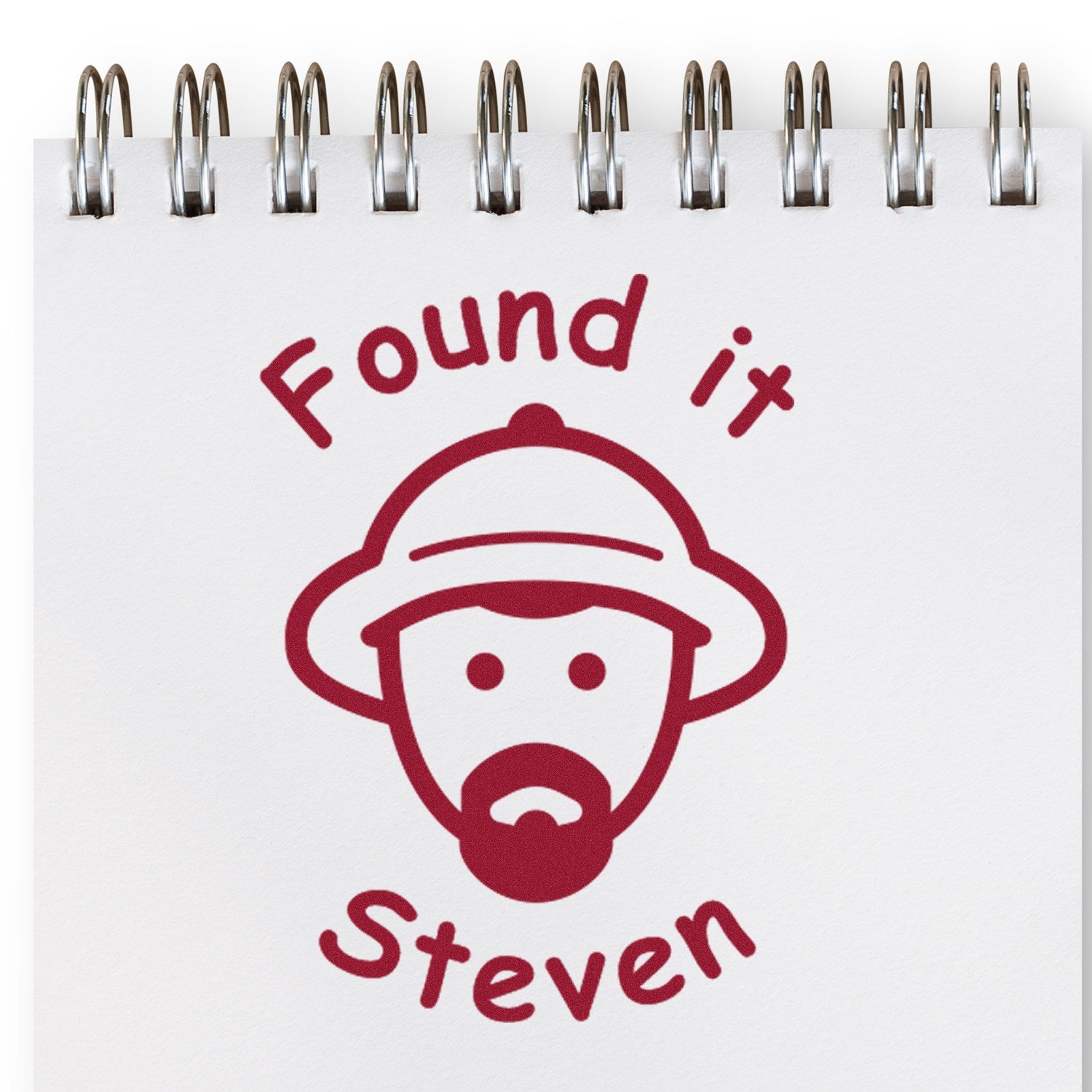 Red stamp seal on white spiral notebook page, reading Found it Steven with a bearded face icon.