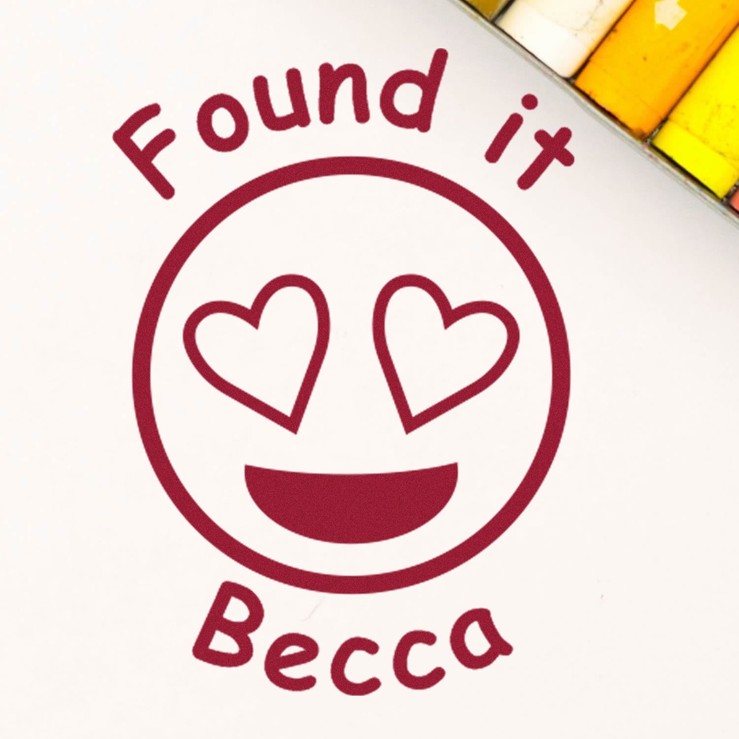 Maroon Found it Becca stamp seal with heart eyes smiley on white, accented by yellow and orange swatches.